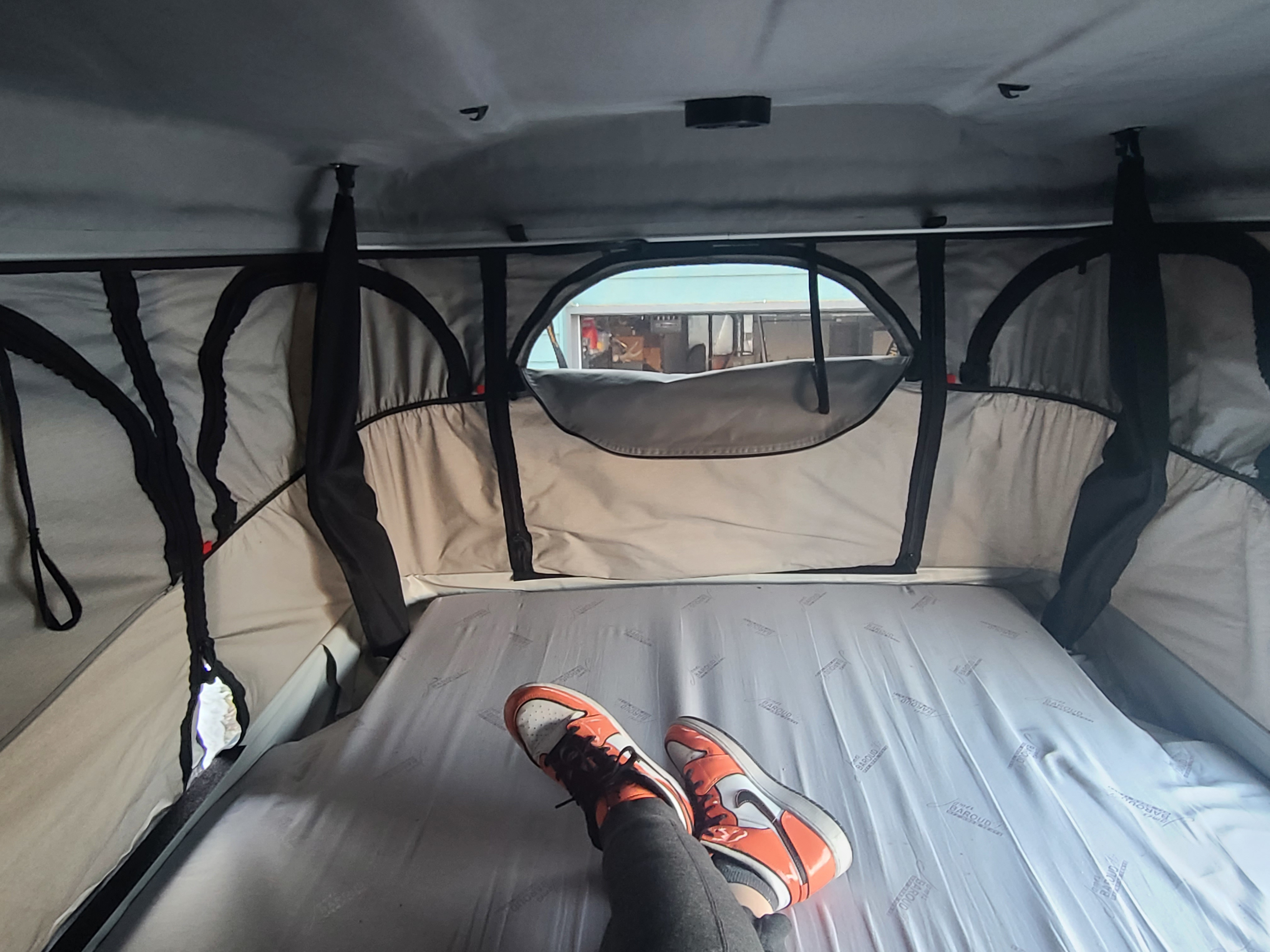 Relaxing inside an RV rental's pop-up tent. A person's feet in orange sneakers rest on the bed, with an outside view.. Dodge Mini C 2017
