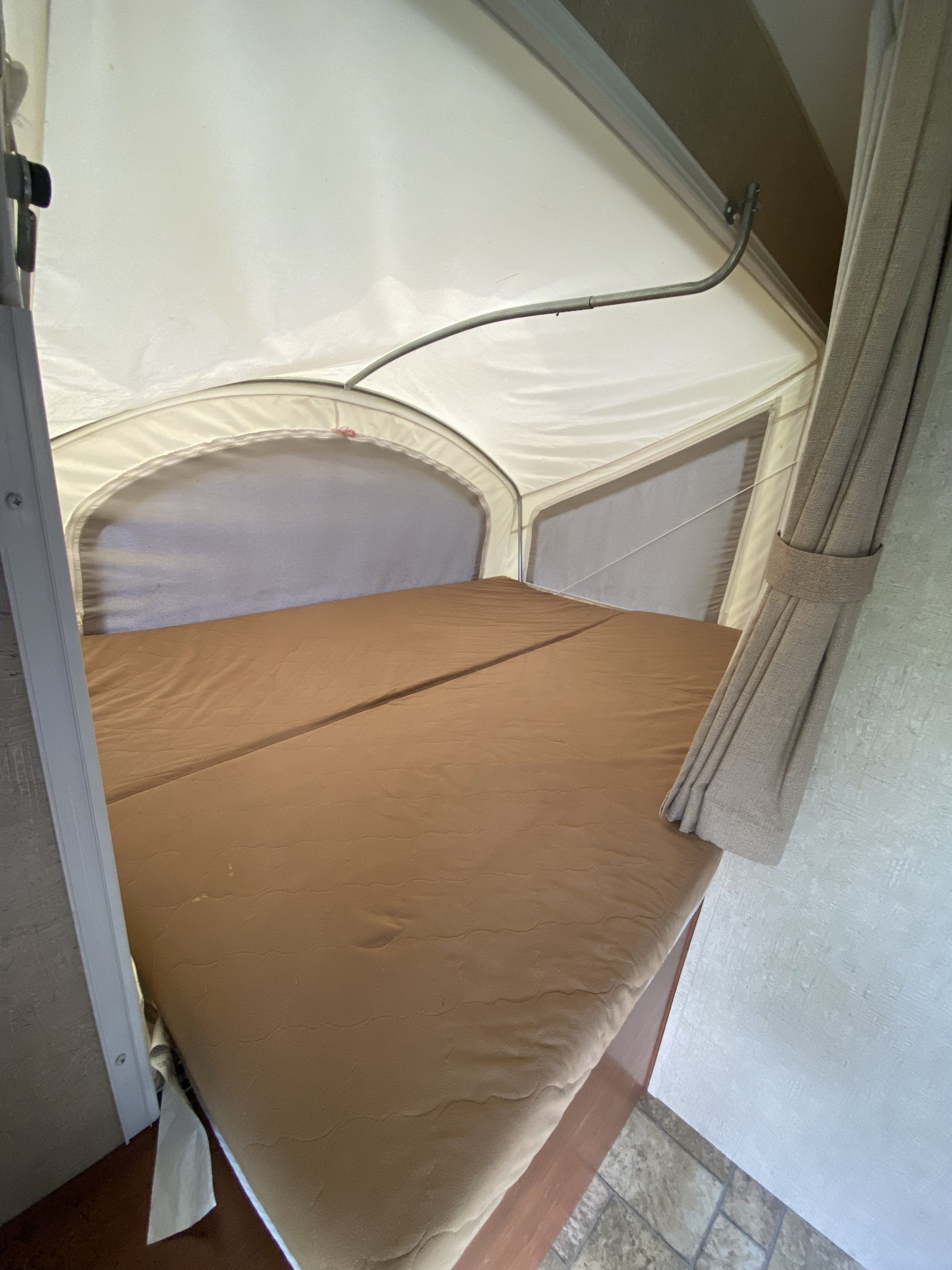 Interior view of an RV rental pop-up camper bed, featuring a brown mattress, canvas walls, and windows for sleeping.. KZ Sportsman 2013