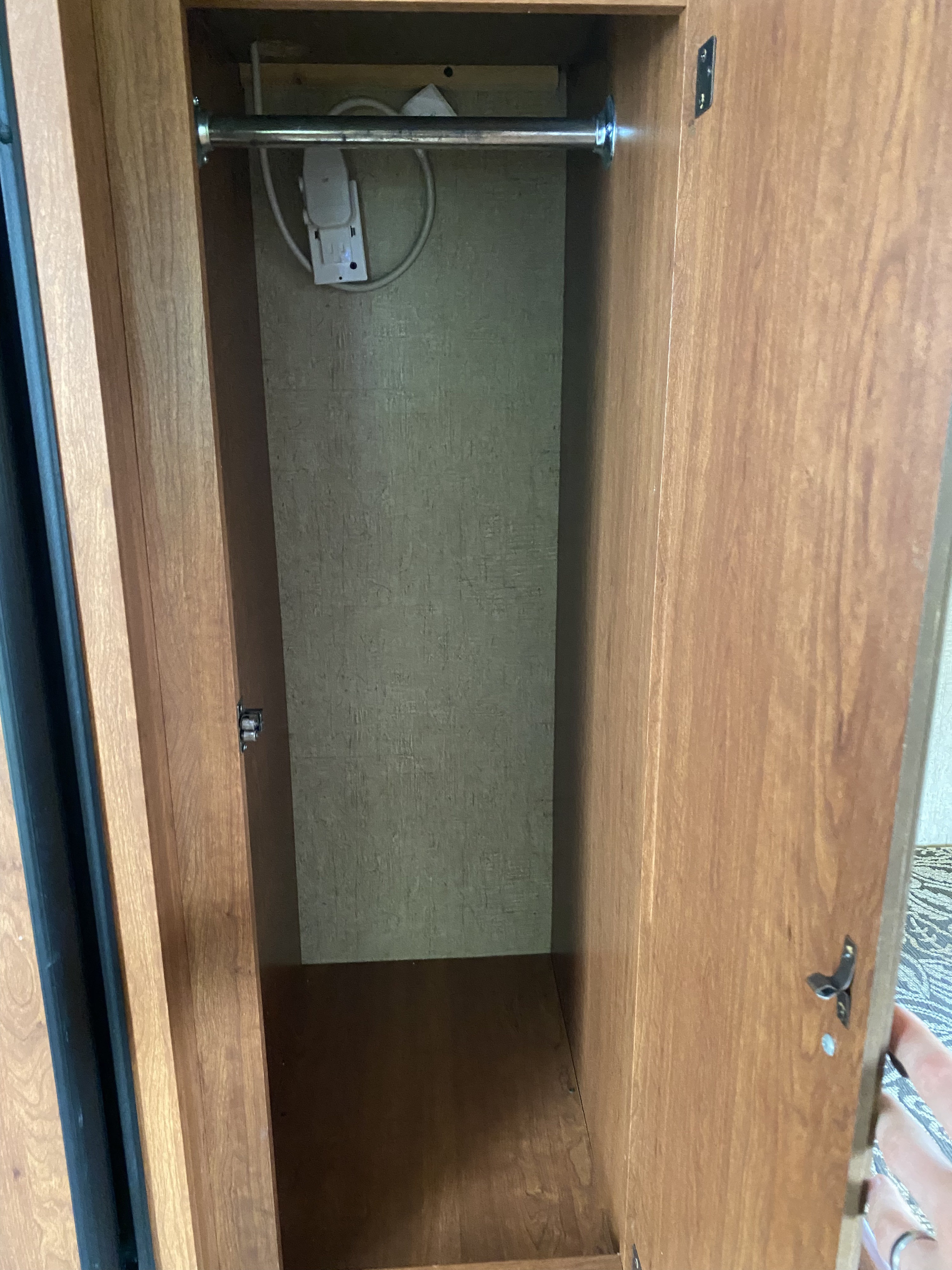 Empty wooden closet in an RV rental, featuring a metal hanging rod and a power strip for convenience.. KZ Sportsman 2013