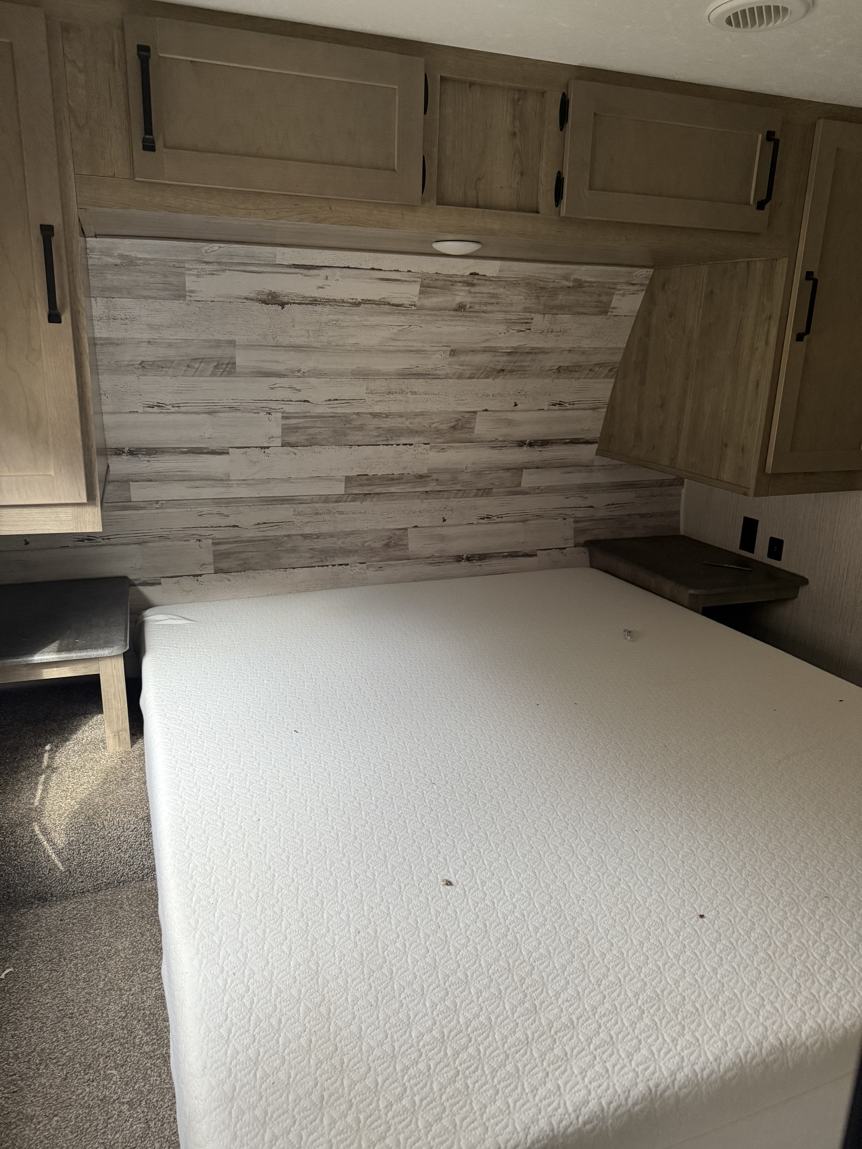 Cozy RV rental bedroom with white mattress, overhead storage cabinets, and rustic wood-look headboard.. Puma Unleashed Unleashed toy hauler 2021
