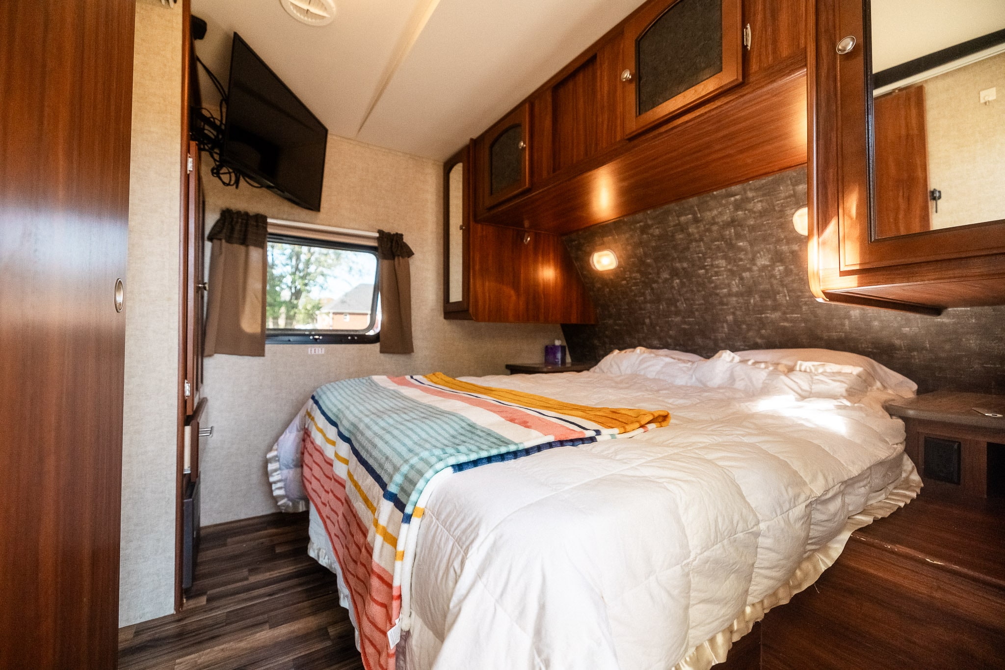 Comfortable RV rental bedroom with a cozy bed, overhead cabinets, and TV, offering a relaxing stay.. Heartland RVs North Trail 2015