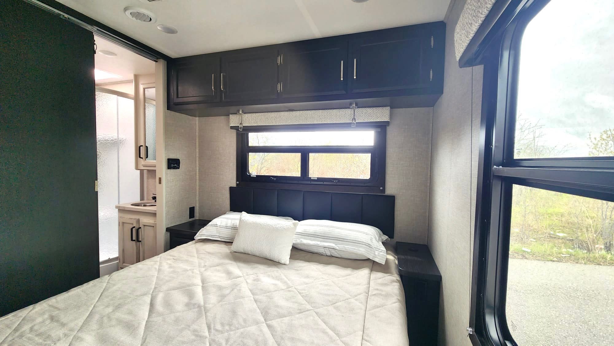 Modern RV rental bedroom with a comfy bed, window view, overhead storage, and adjacent bathroom.. JAYCO REDHAWK 2023 2023