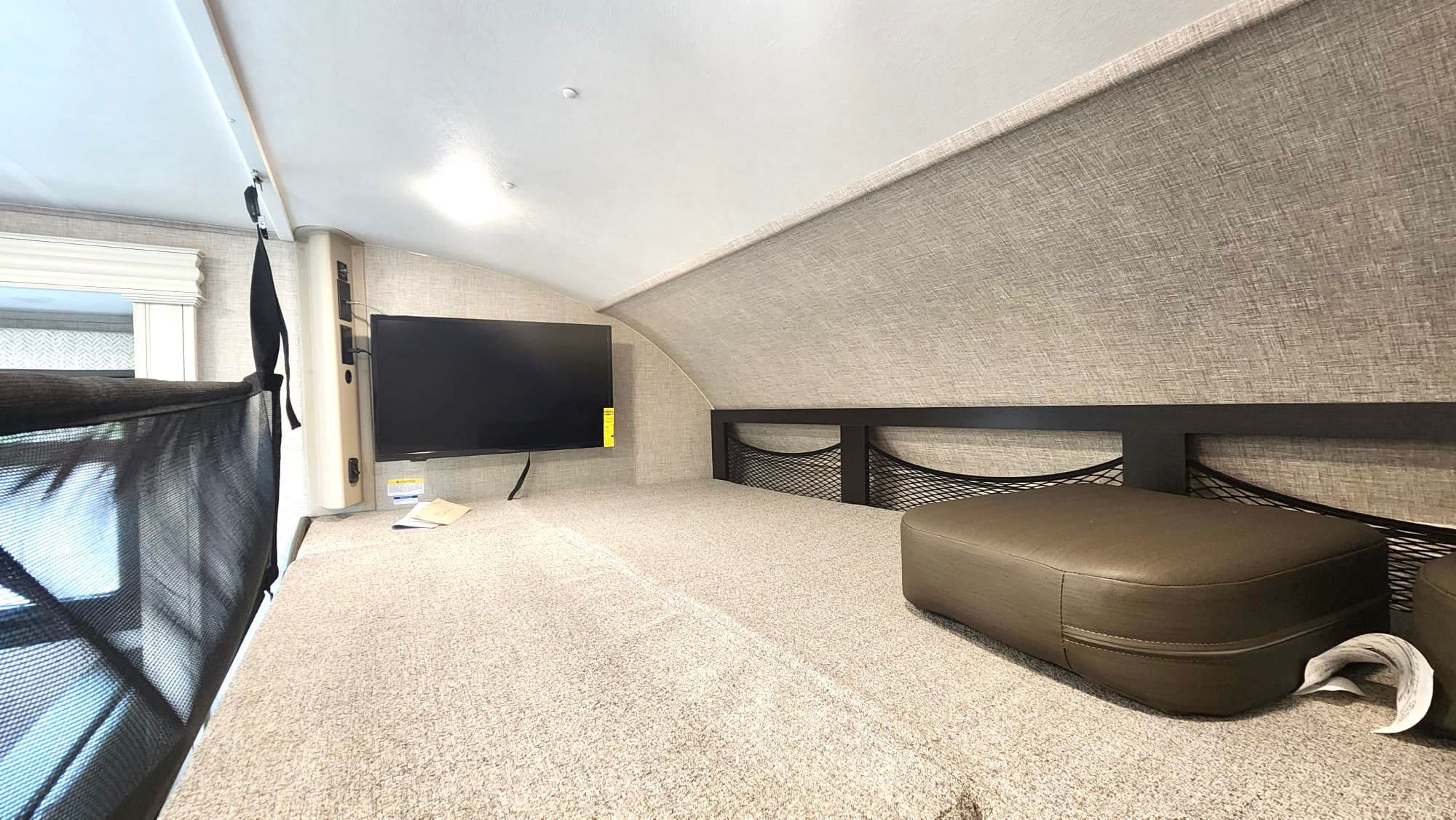 Spacious RV rental bunk with a mounted TV, safety net, and mesh storage. Ideal for comfortable travel.. JAYCO REDHAWK 2023 2023