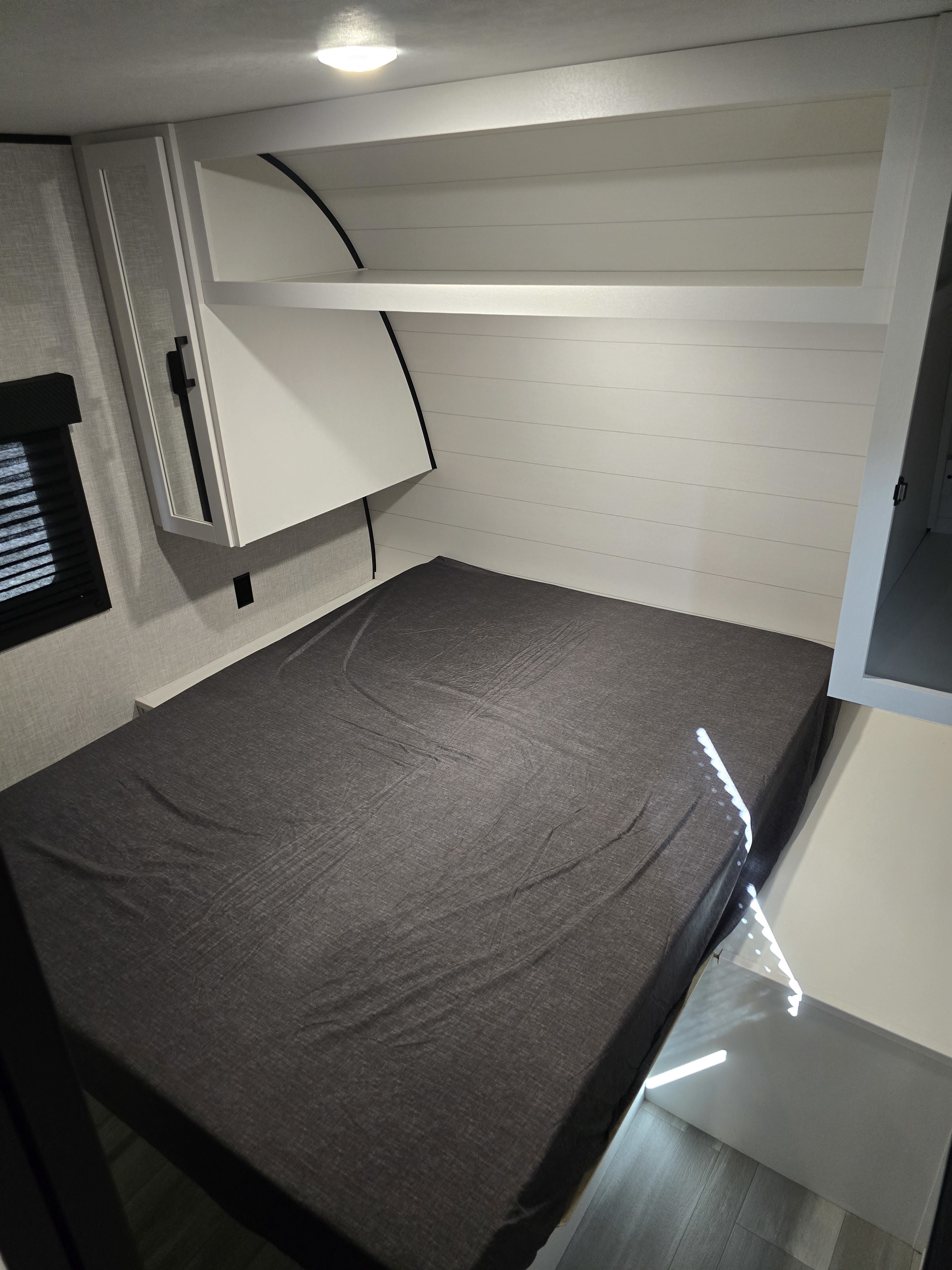Bright RV rental bedroom: dark gray bed, white shiplap walls, modern overhead cabinets, and a window with blinds.. Starcraft Autumn Ridge 26BH 2025