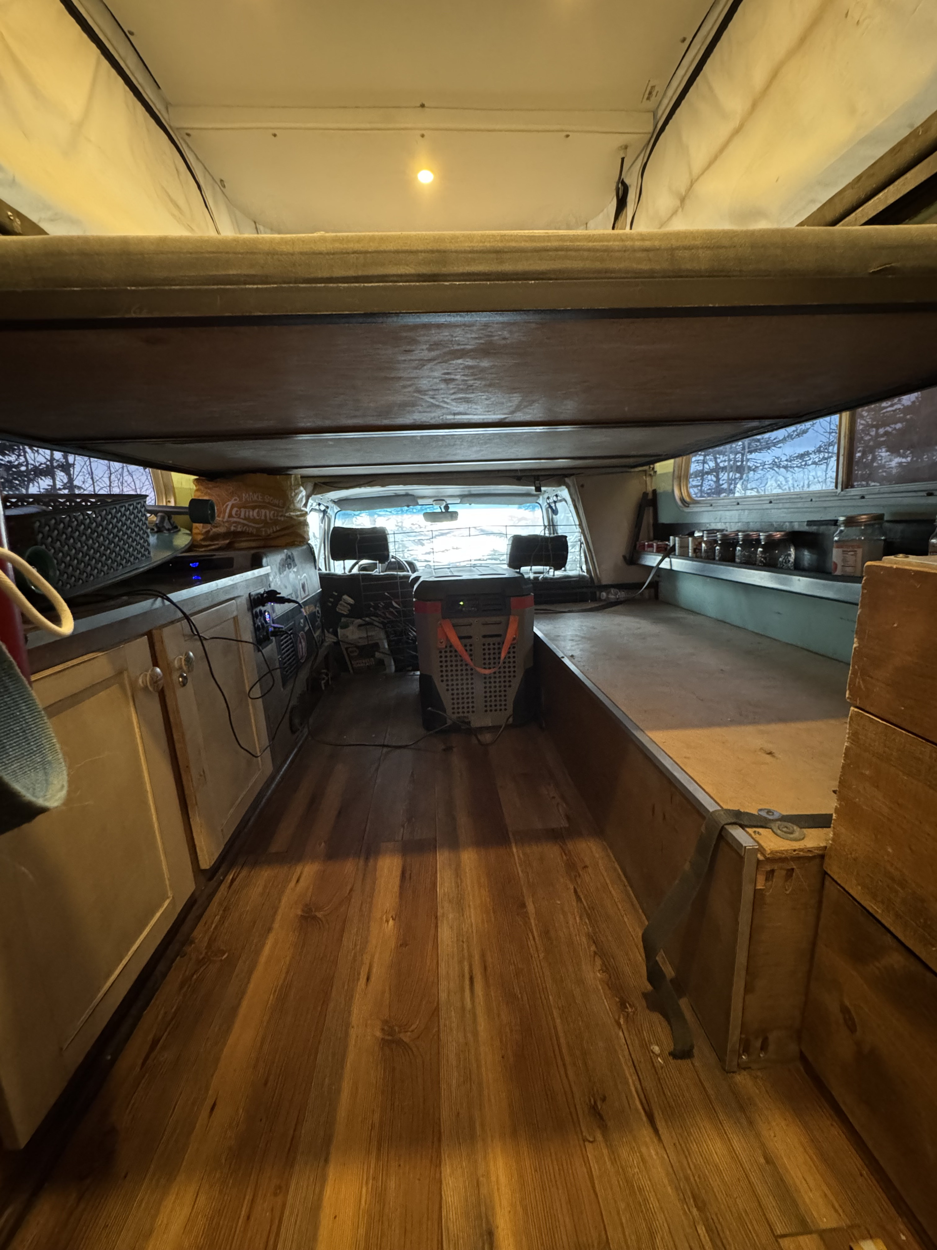 View into an RV rental with wood floors. Features include a kitchen counter, portable fridge, and a built-in sleeping platform.. Toyota Hilux 1982