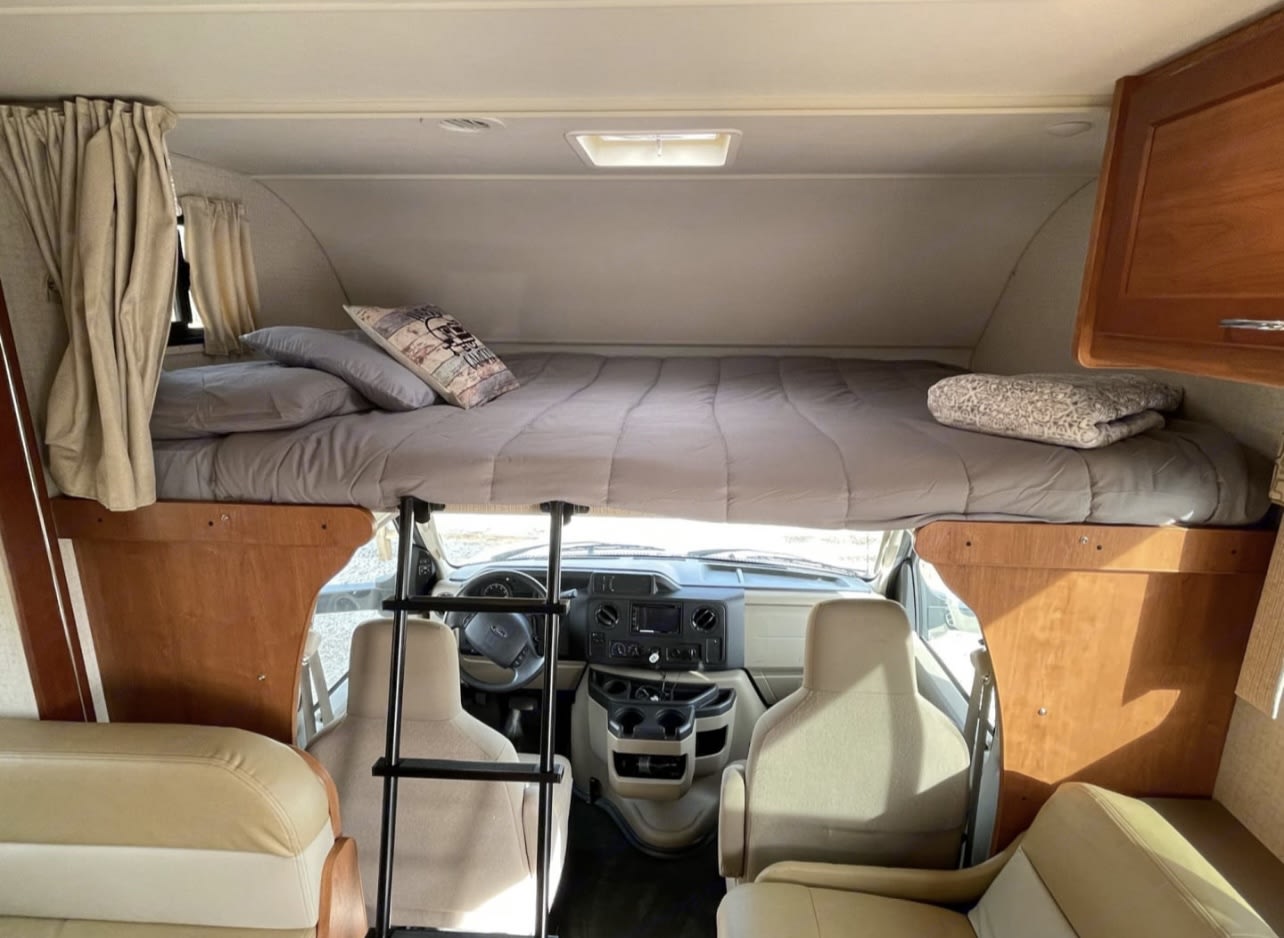 RV rental interior: Comfortable bed above the driver's cabin, with a ladder for access. Driver/passenger seats visible below.. Winnebago Minnie Winnie 2017