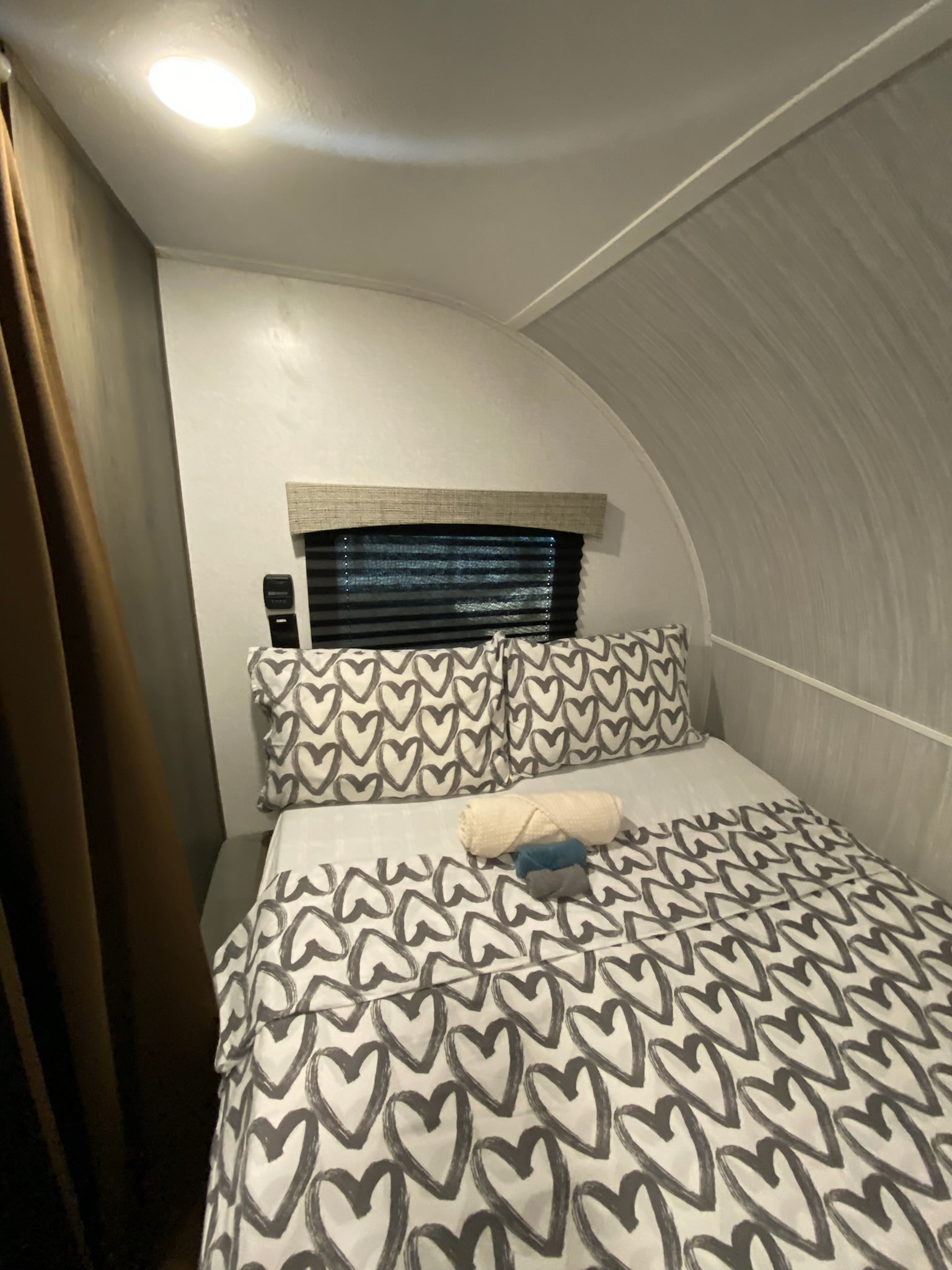 RV rental bedroom: cozy bed with heart-patterned bedding, window, and warm overhead light in a curved interior.. Forest River Viking TD 2023