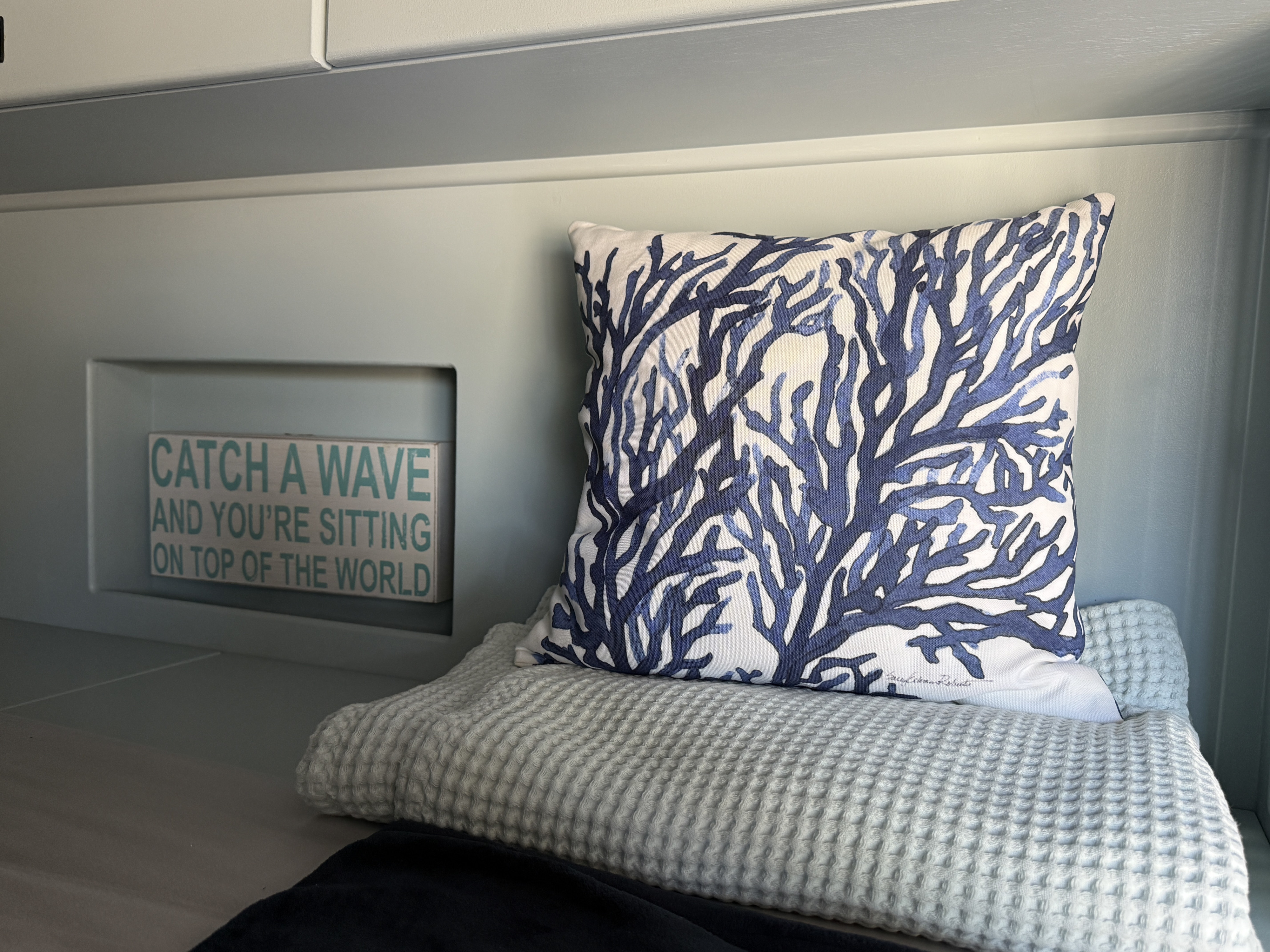 Cozy RV rental interior with blue coral pillow, soft waffle blanket, & "Catch a Wave" sign.. Dodge RAM Promaster HR 159 WB 2022