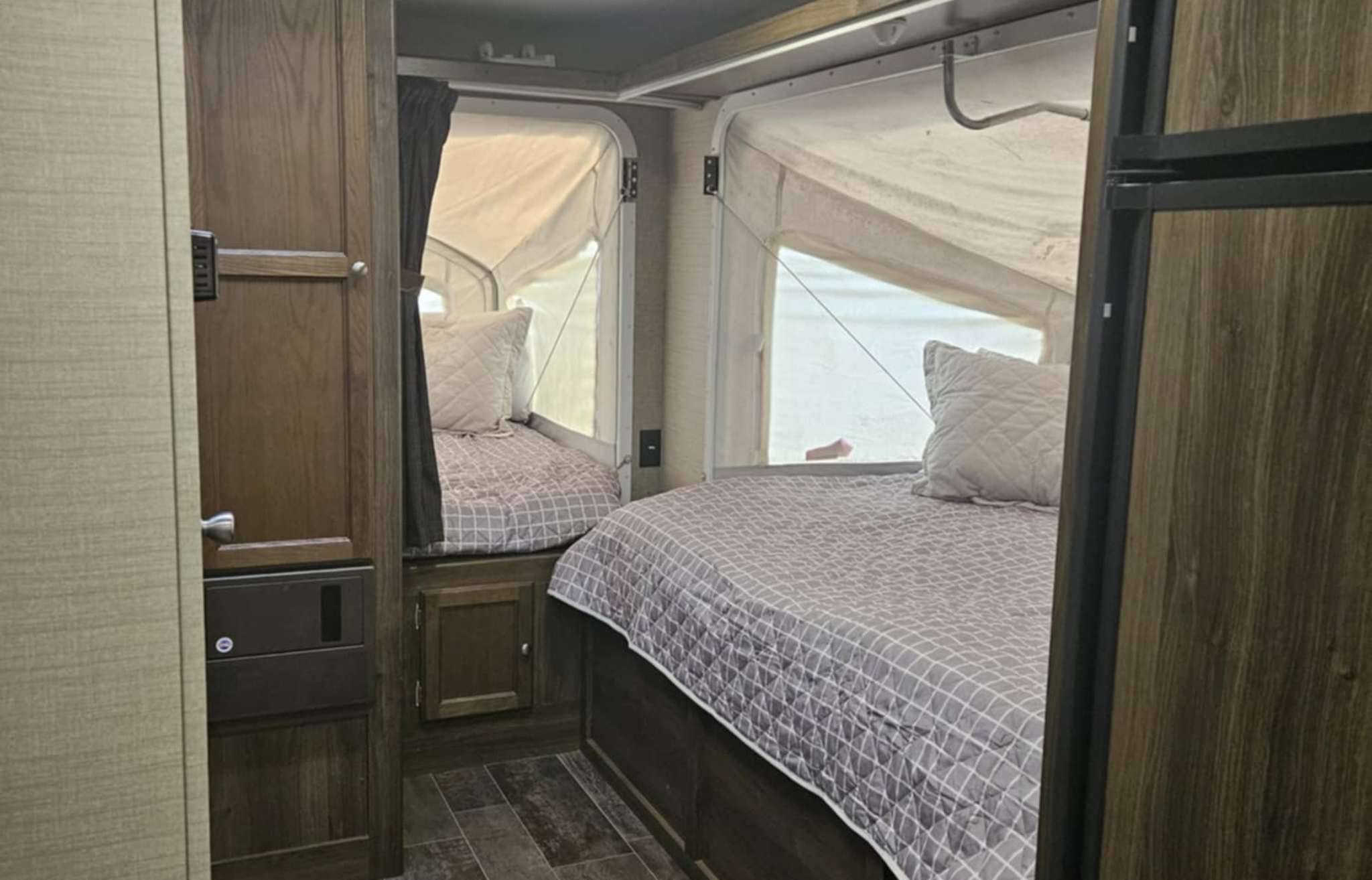 RV rental interior: two beds in pop-out canvas sections with cozy bedding, wood cabinets, and durable flooring, offering a unique sleep space.. Keystone Bullet 2017