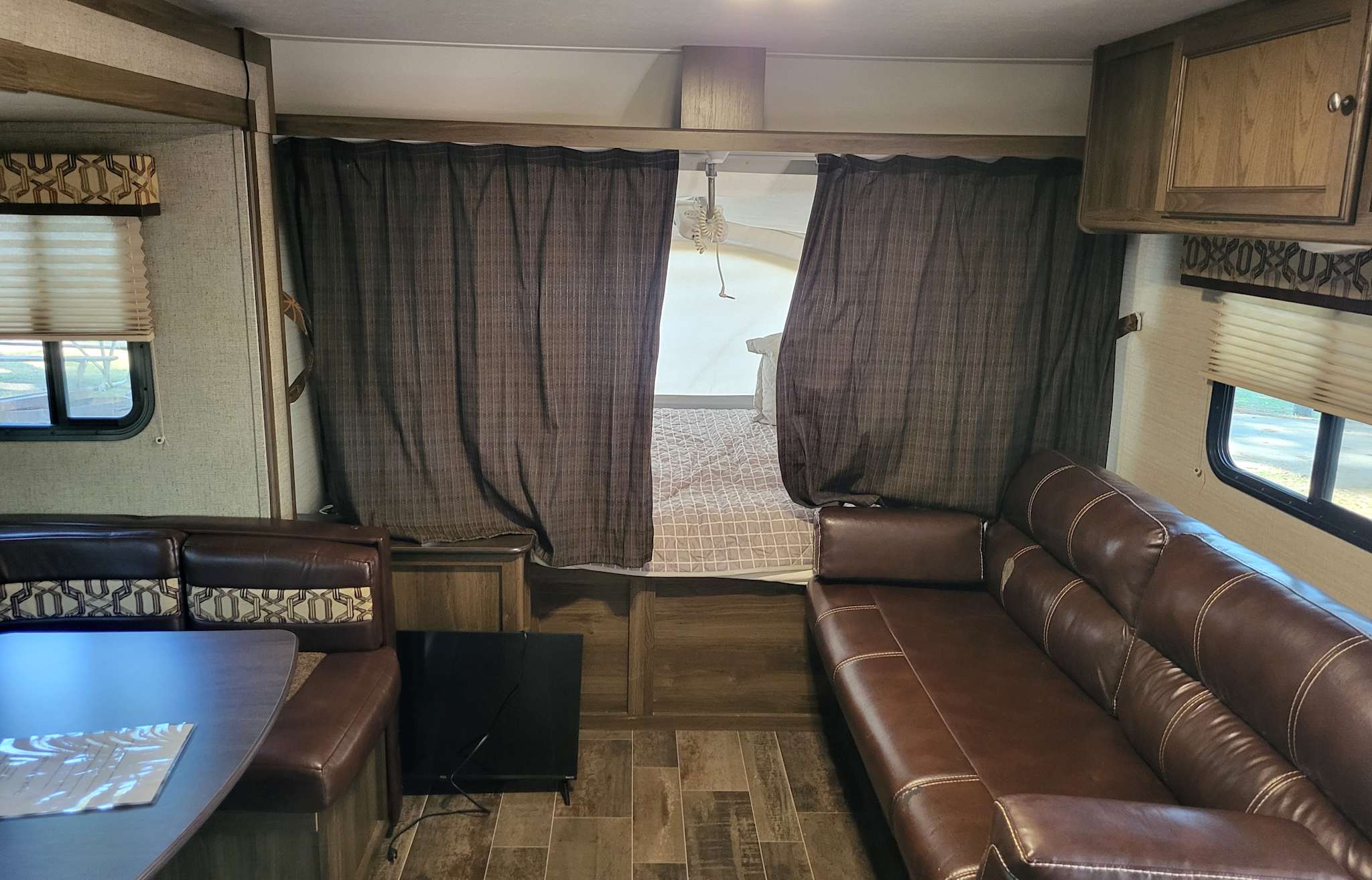 Comfortable RV rental interior with brown leatherette seating, wood-look flooring, and privacy curtains for the sleeping area.. Keystone Bullet 2017