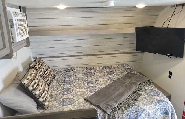 This cozy RV rental bedroom features a comfy bed with decorative pillows, a wall-mounted AC unit, and a TV.. Dutchmen Coleman 2023