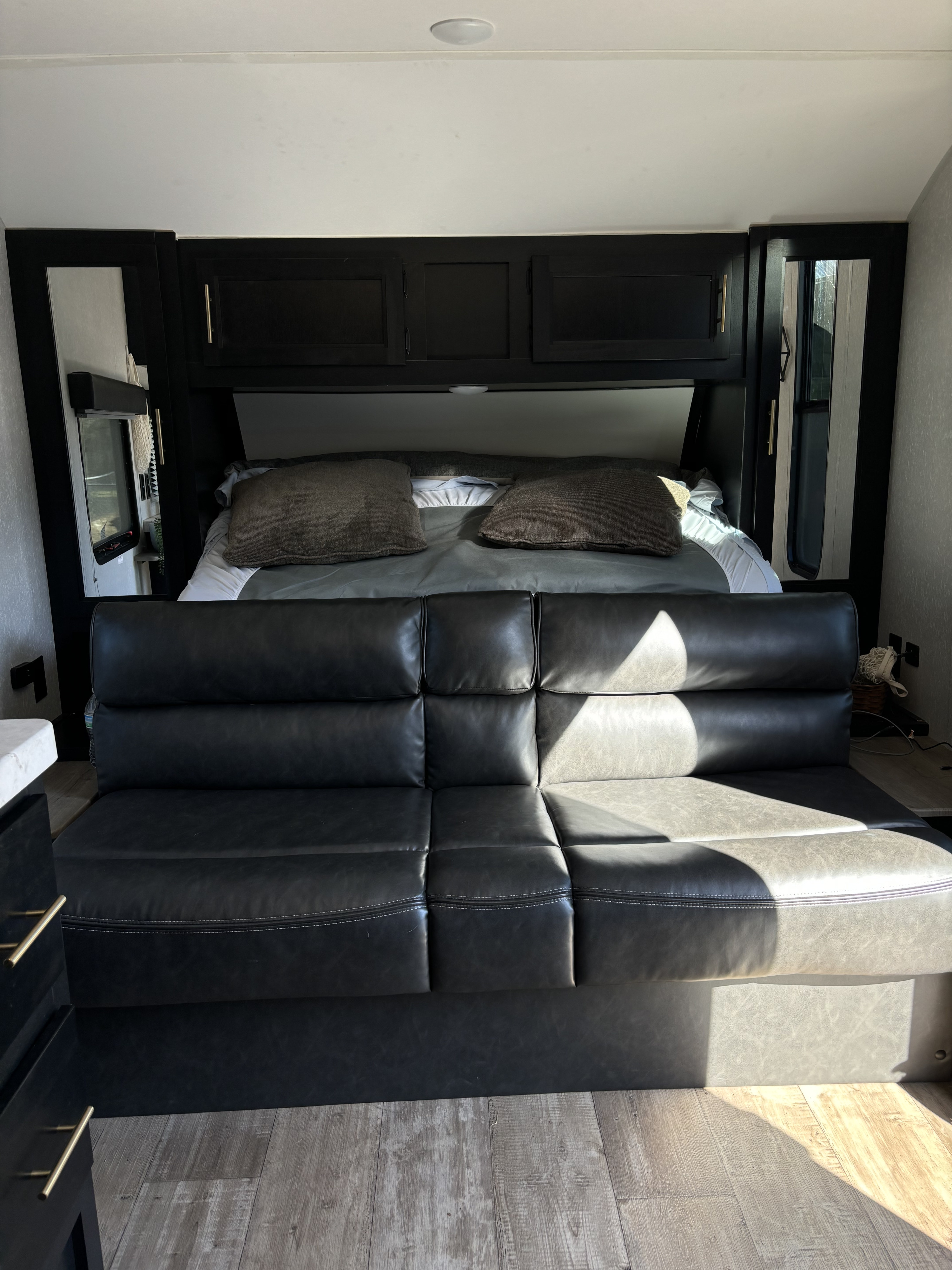 RV rental interior featuring a versatile black leather sofa that converts to a bed, overhead cabinets, and comfy bedding.. Forest River Cherokee Grey Wolf 2022