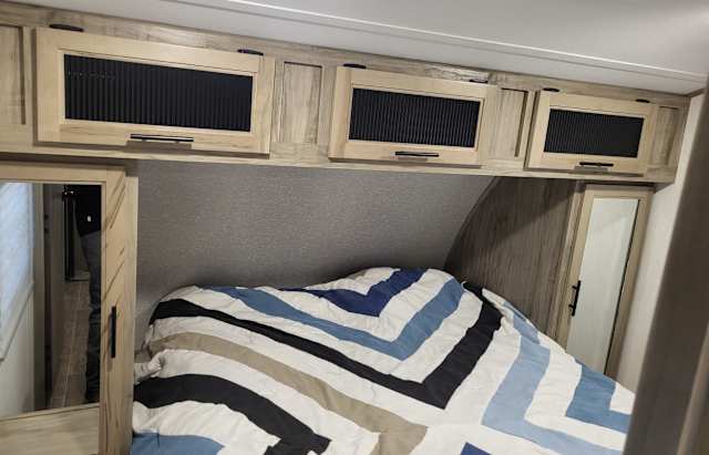 Cozy RV rental bedroom featuring a striped bed, overhead storage cabinets, and mirrored wardrobes.. Forest River Cherokee Alpha Wolf 2022
