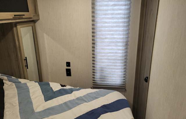 RV rental bedroom interior: blue/white striped bed, window blinds, and wood cabinetry with mirror. Cozy travel space.. Forest River Cherokee Alpha Wolf 2022