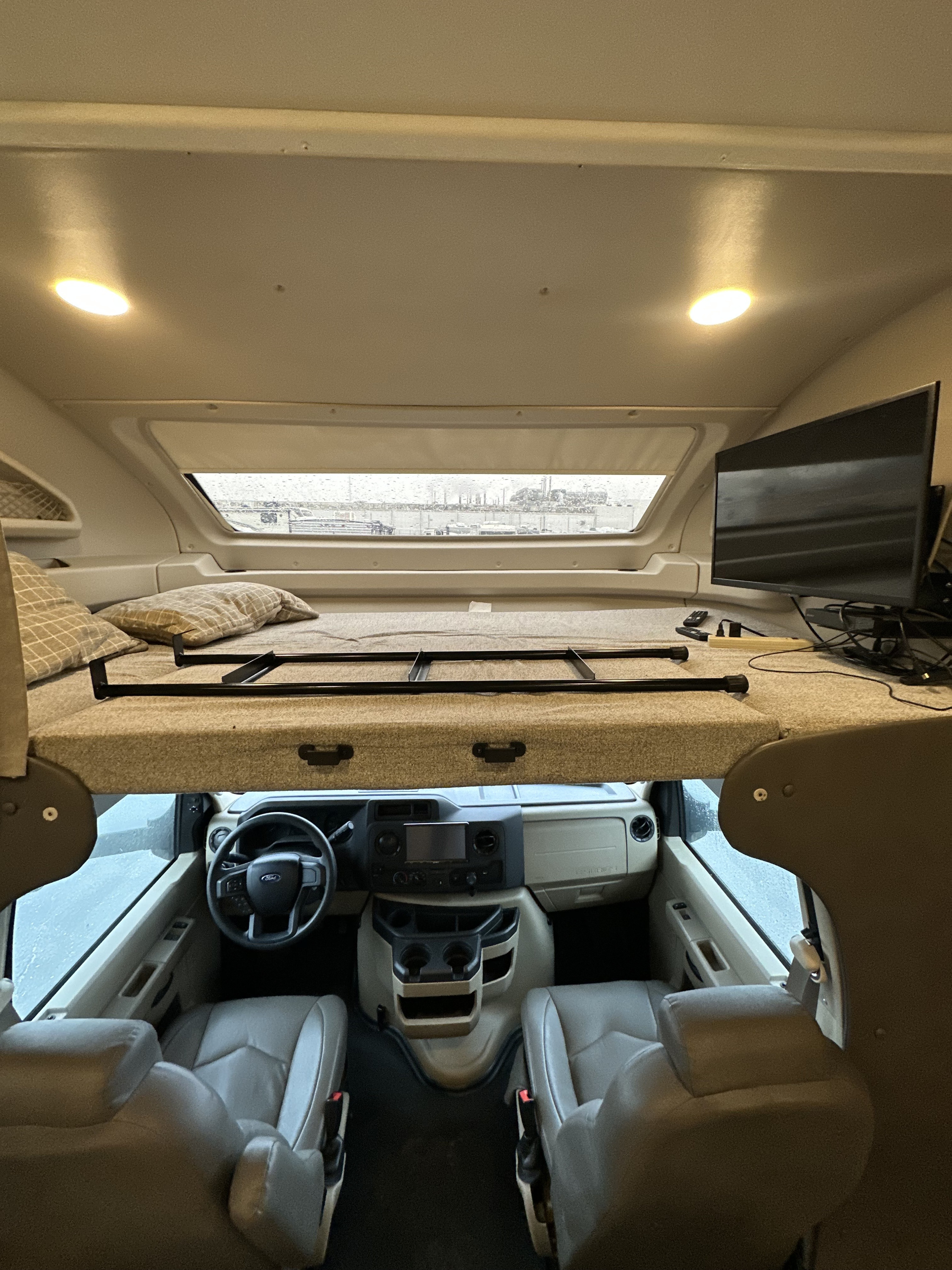 RV rental interior showing a cozy bunk bed above the cab, with a TV and rainy window view of the outside.. Entegra Esteem 29V 2021