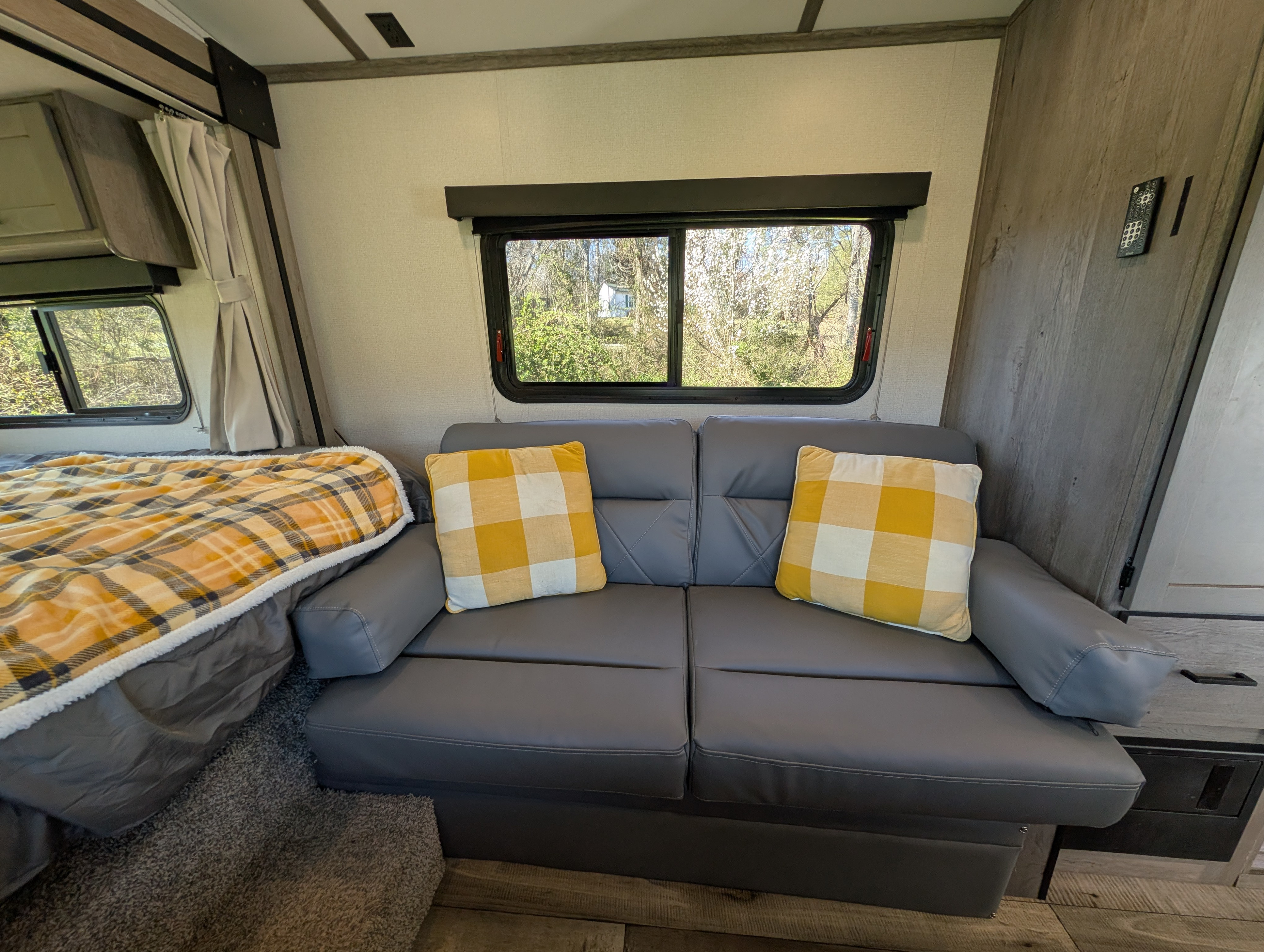 Step inside this comfy RV rental, featuring a grey sofa, plaid accents, a cozy bed, and bright windows.. Keystone Outback Ultra Lite 2021