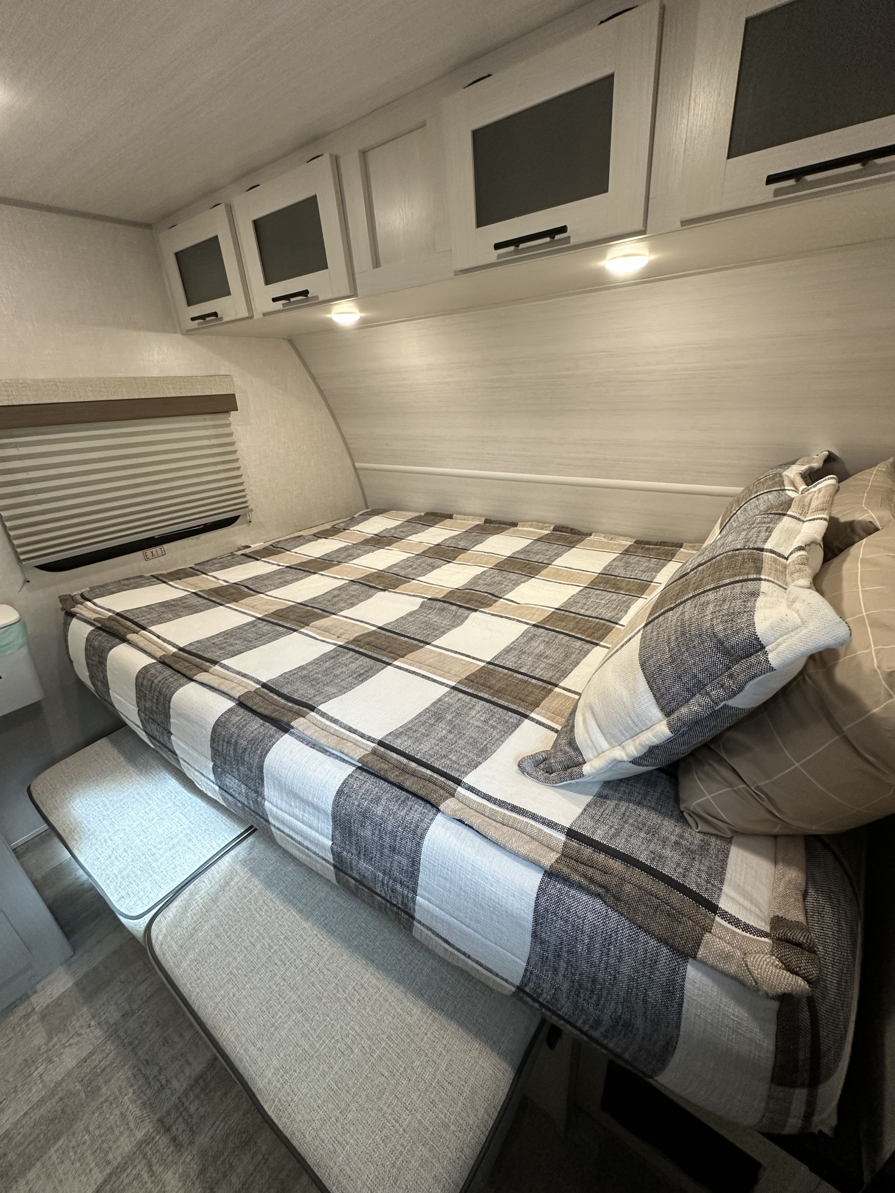 Cozy RV rental bedroom interior with plaid bedding, overhead cabinets, and window. Ideal for adventures!. No Boundaries 19.3 EO 2024