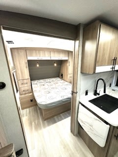 Modern RV rental interior: A comfortable bedroom with a bed is seen through a doorway, with a compact kitchen area to the right.. Grand Design Imagine 2024
