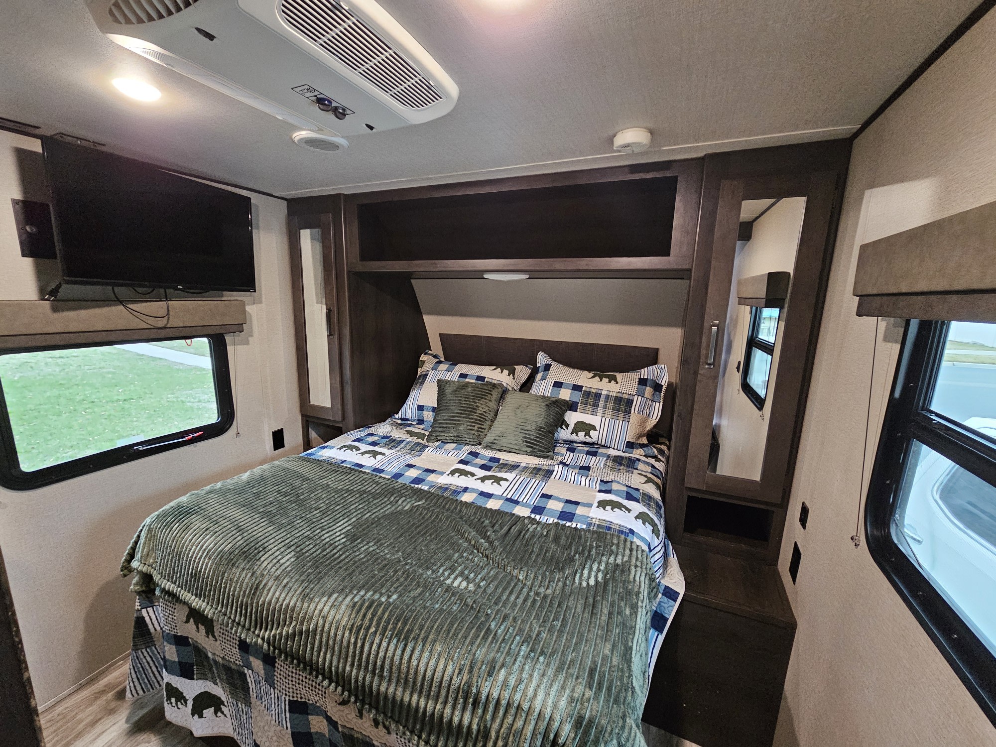 Cozy RV rental bedroom with bear-themed bedding, a wall-mounted TV, overhead AC, and storage cabinets.. Grand Design Transcend Xplor 2022