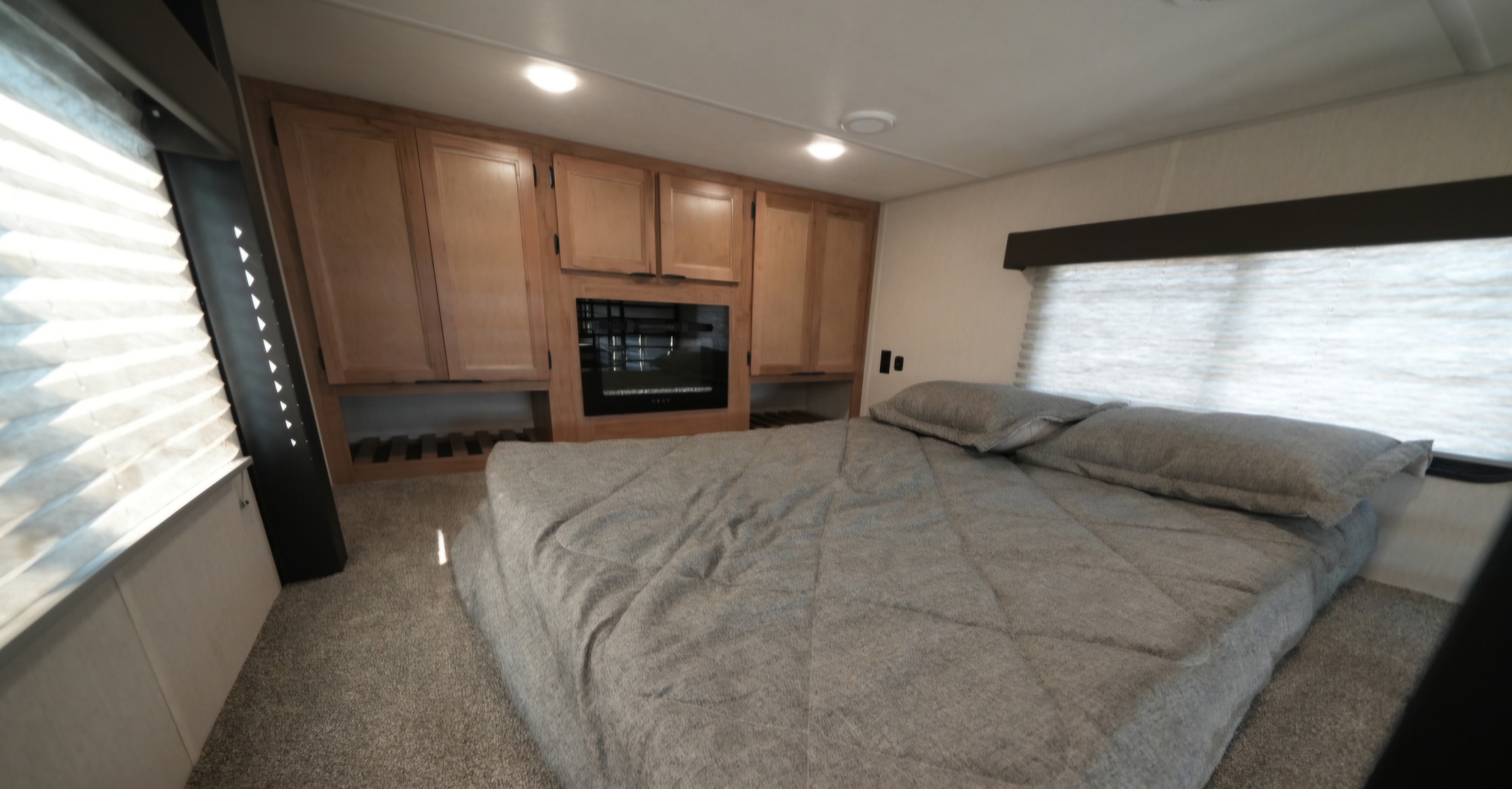 This RV rental bedroom features a cozy bed, built-in wooden cabinets with a fireplace, and bright pleated window blinds.. Forest River Cherokee Timberwolf 16ML 2024