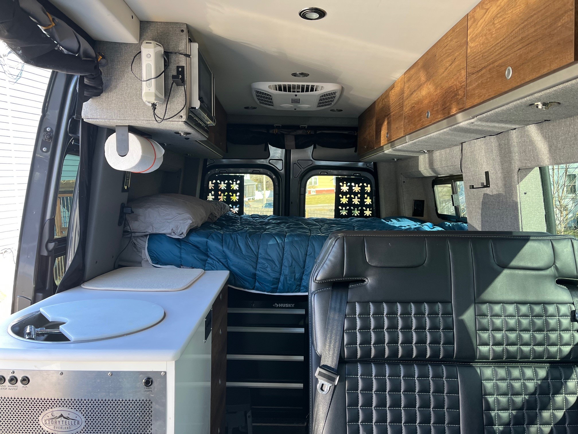 Explore this RV rental's interior: comfy bed, integrated kitchen, and ample storage, perfect for your next road trip.. Storyteller Overland Stealth Mode 2023