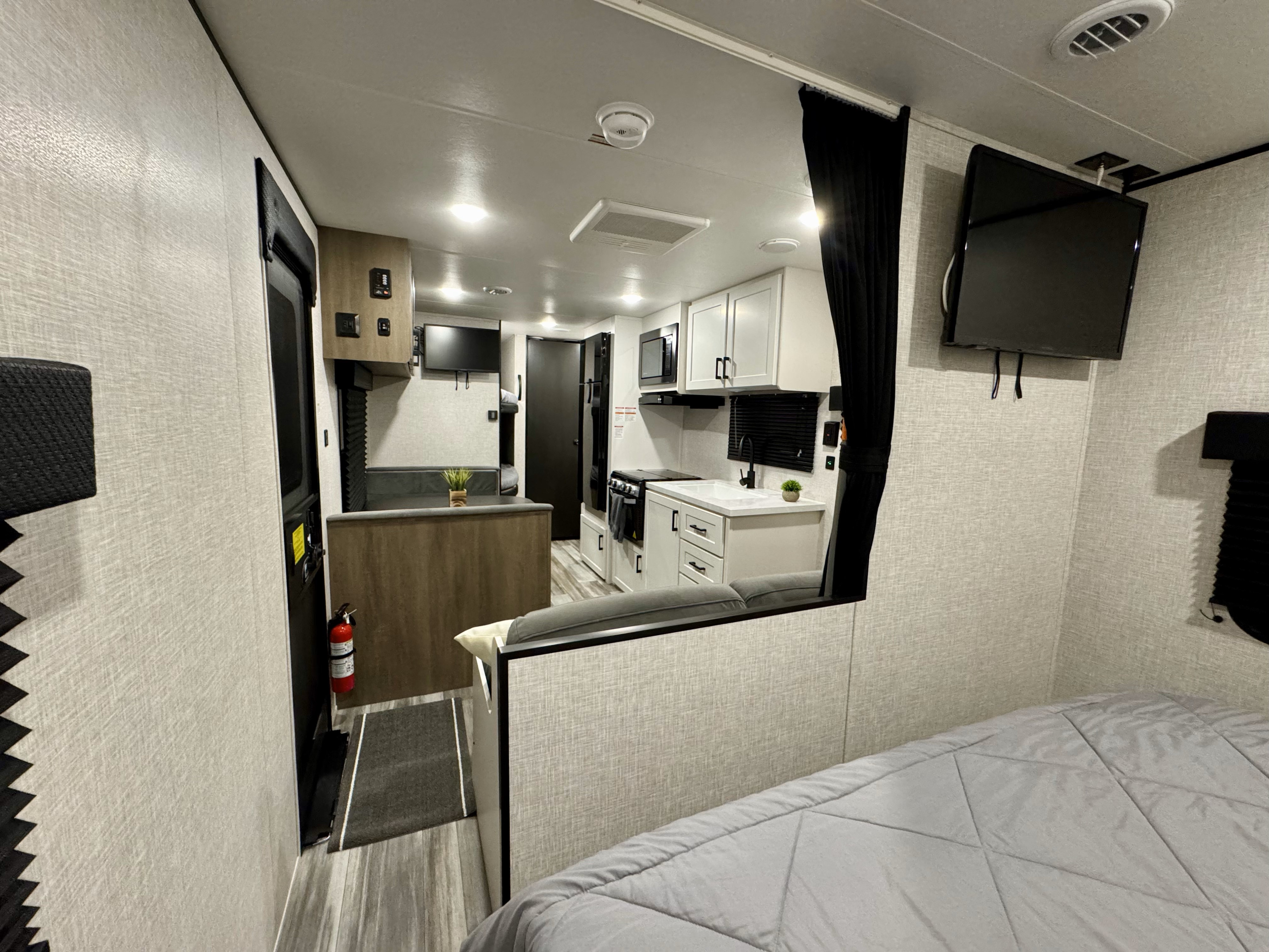 Inside a modern rv rental: bright kitchen with white cabinets, dining booth, and bedroom area. Fire extinguisher visible.. Jayco 260BH 2025