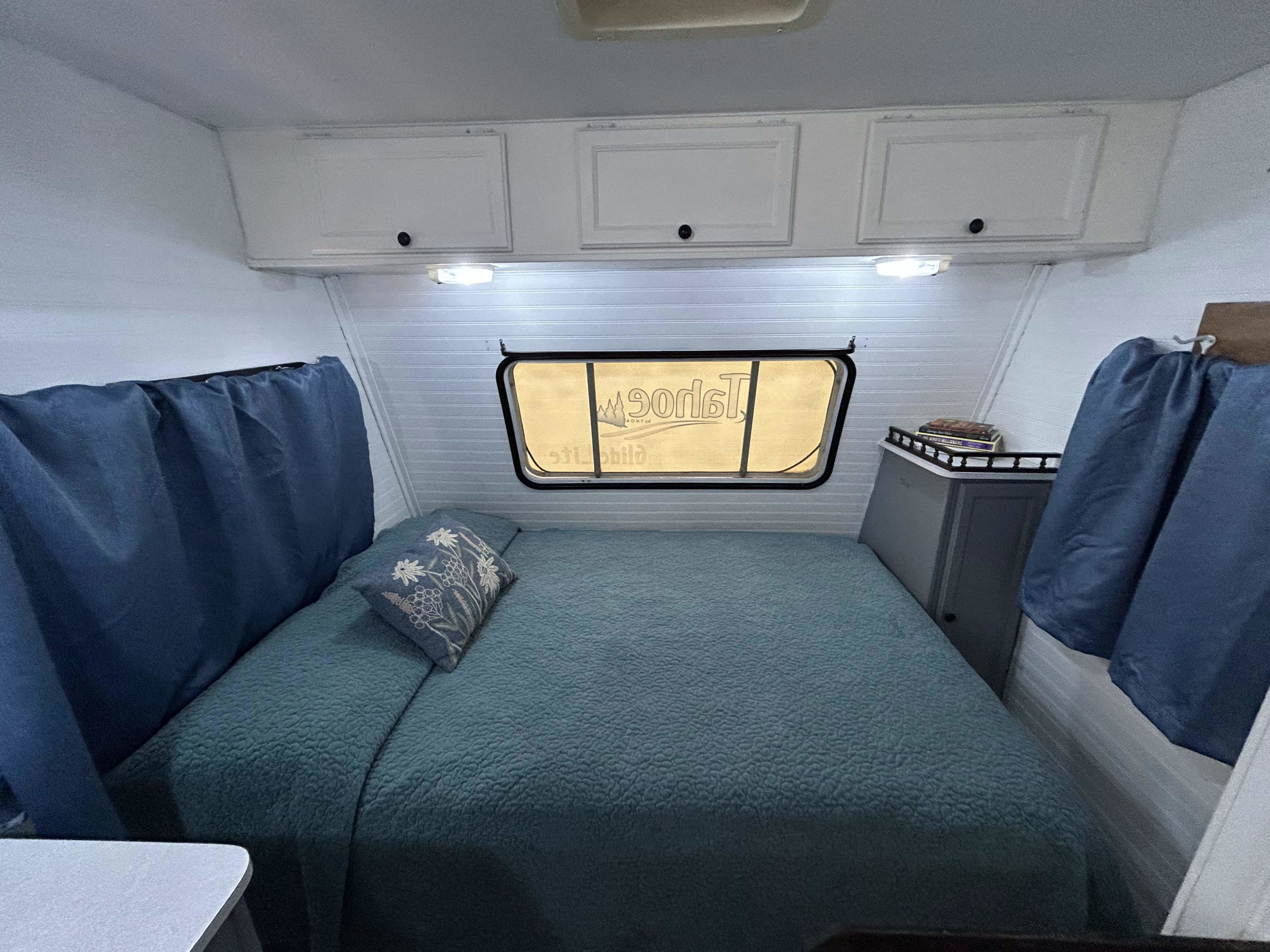 Inside a bright RV rental bedroom, featuring a large bed with a teal quilt, white cabinets, and a window. Perfect for travel.. Thor Motor Coach Tahoe Pak Rat 1998