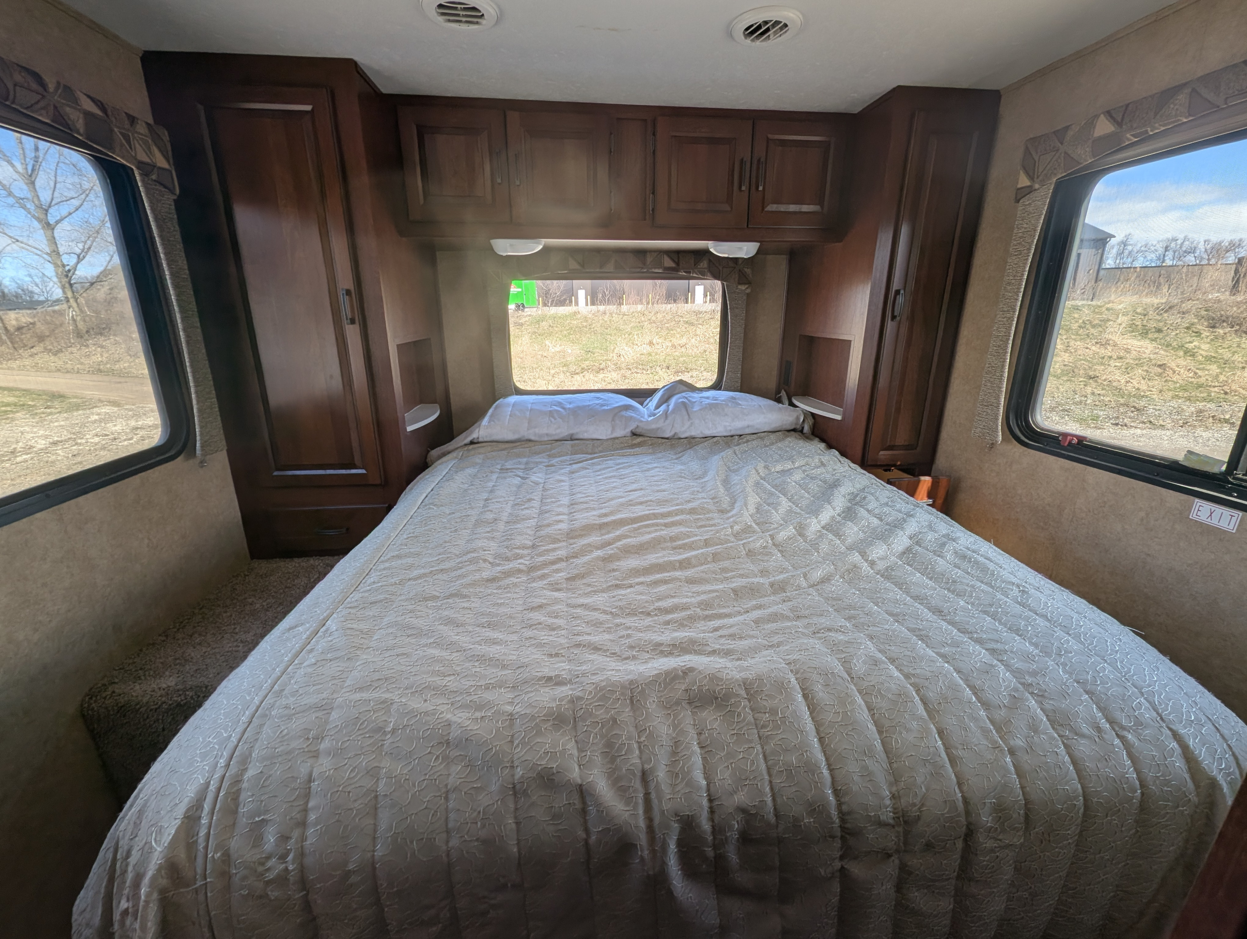 Cozy RV rental bedroom with a bed, wood cabinets, and windows showing outdoor views. Perfect for travel adventures.. Forest River Sunseeker 2014