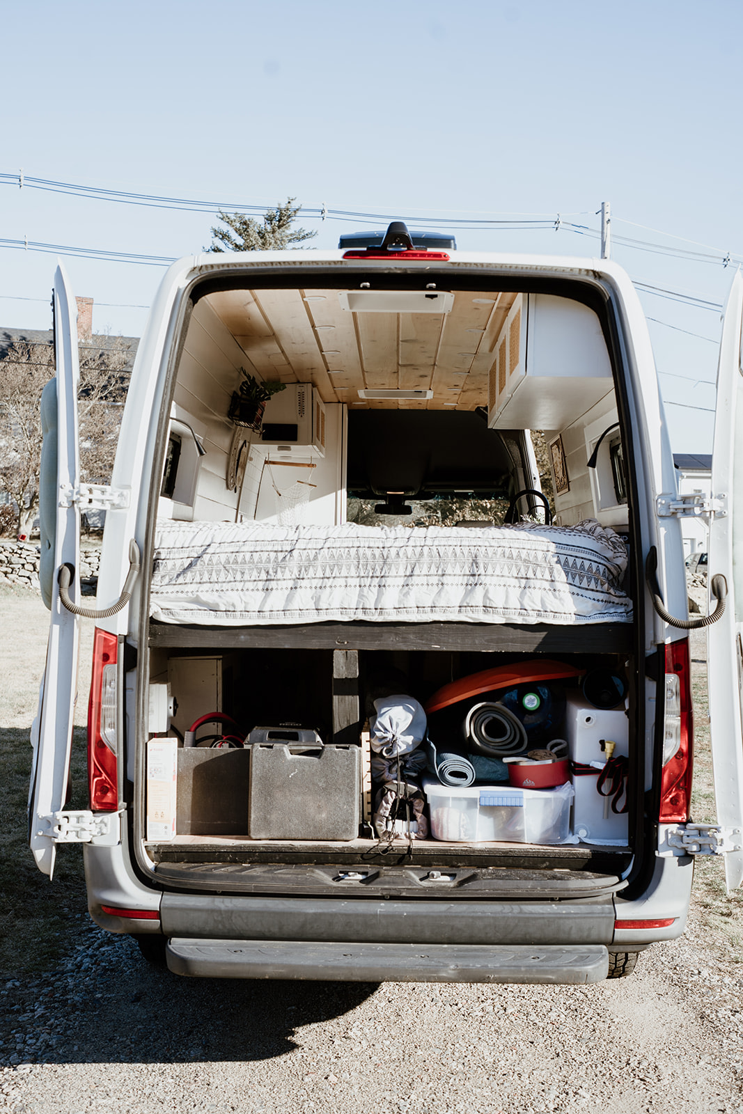 Rear view of an RV rental camper van, showing its organized interior with a raised bed and ample gear storage.. Mercedes Sprinter 2021