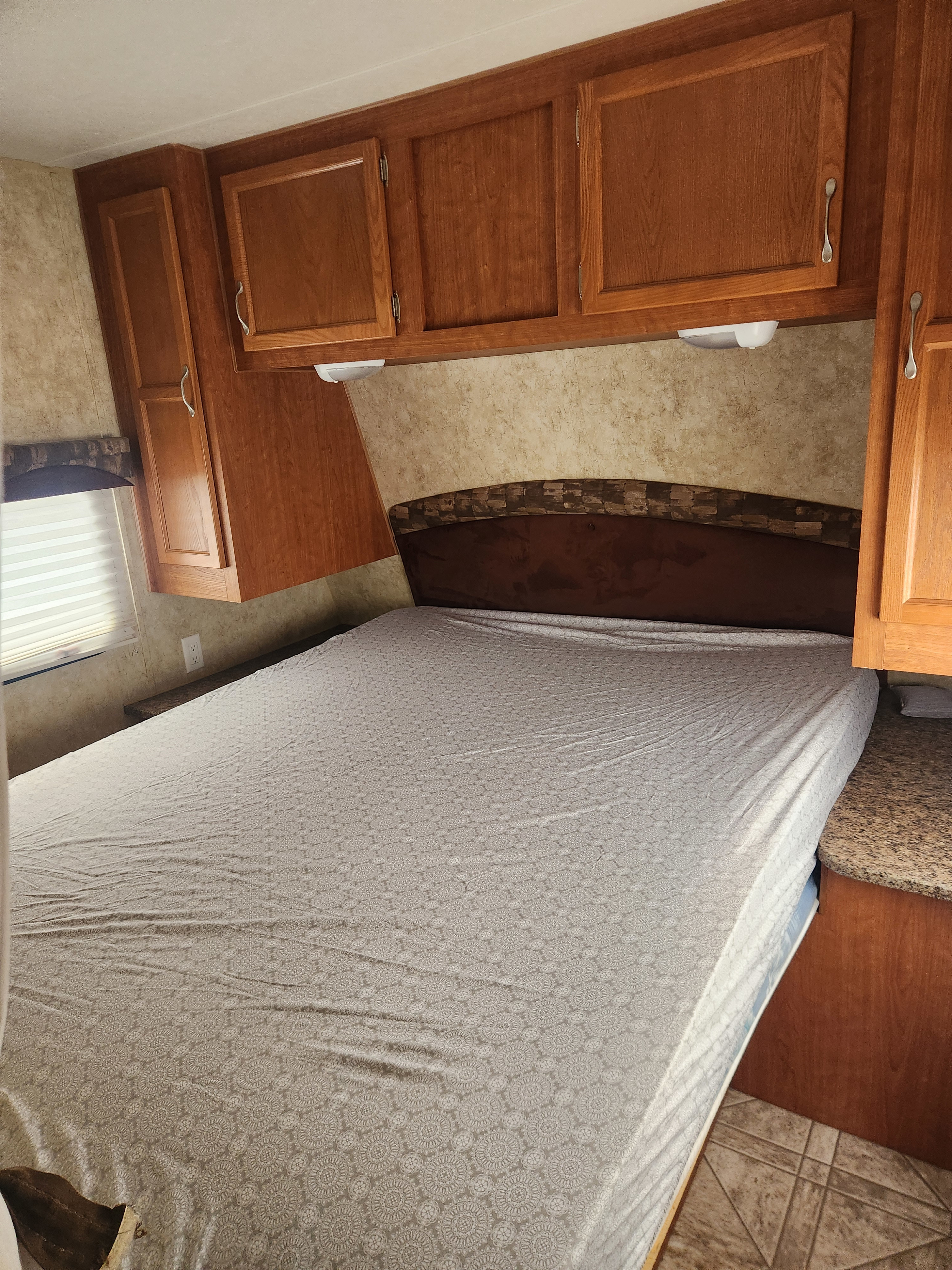 Cozy RV rental bedroom features a comfortable bed with patterned sheets, overhead wooden cabinets, and a padded headboard.. Starcraft Autumn Ridge 2010