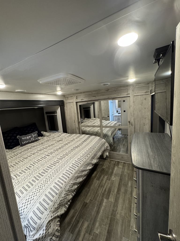 A modern RV rental bedroom offers a patterned bed, mirrored closet, dresser with TV above, and wood floor.. Keystone RV Avalanche 2022