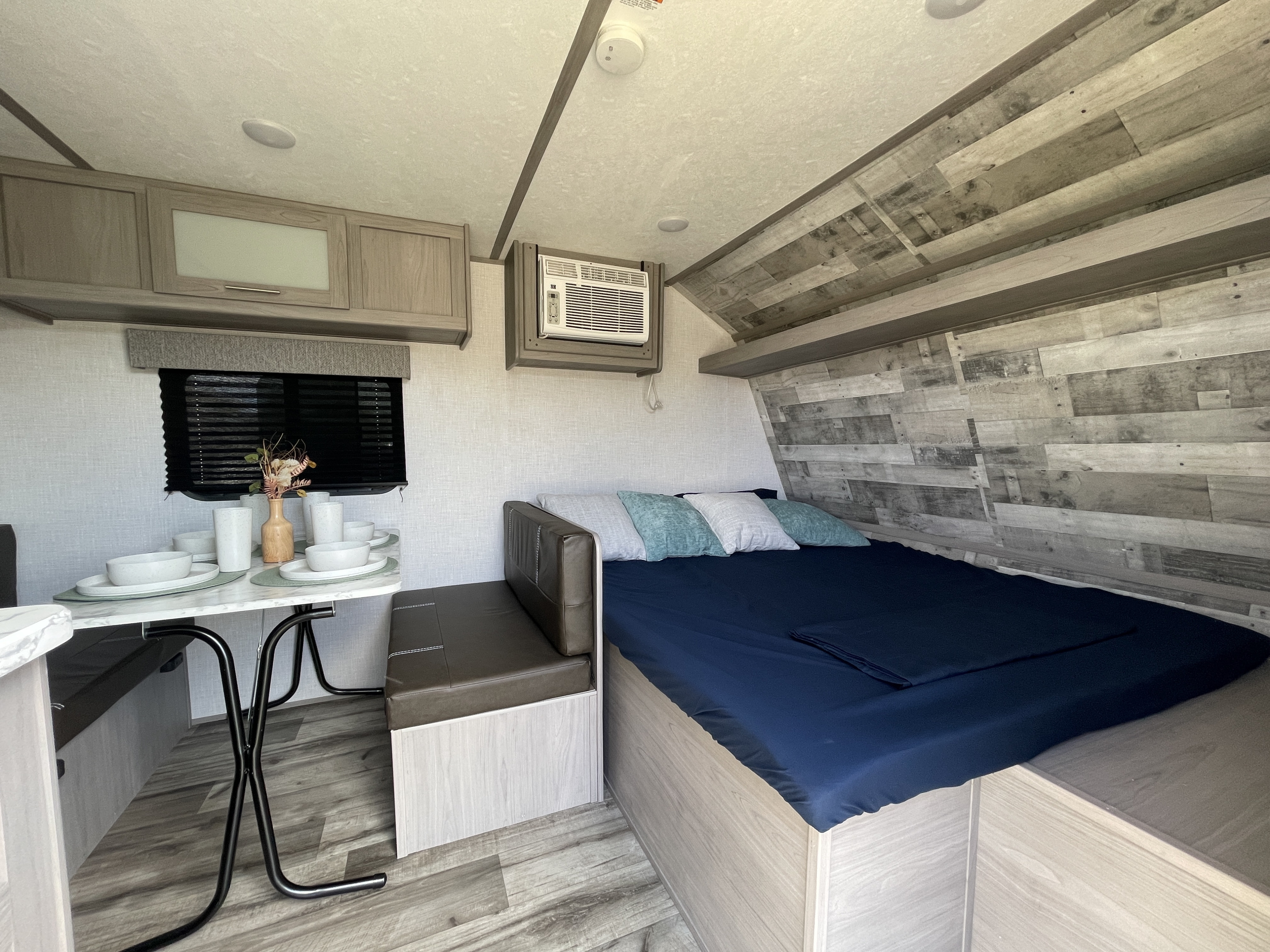 Cozy RV rental interior: bed, dining area with place settings, wall-mounted AC, and overhead cabinets.. Dutchmen Coleman Lantern LT 2023