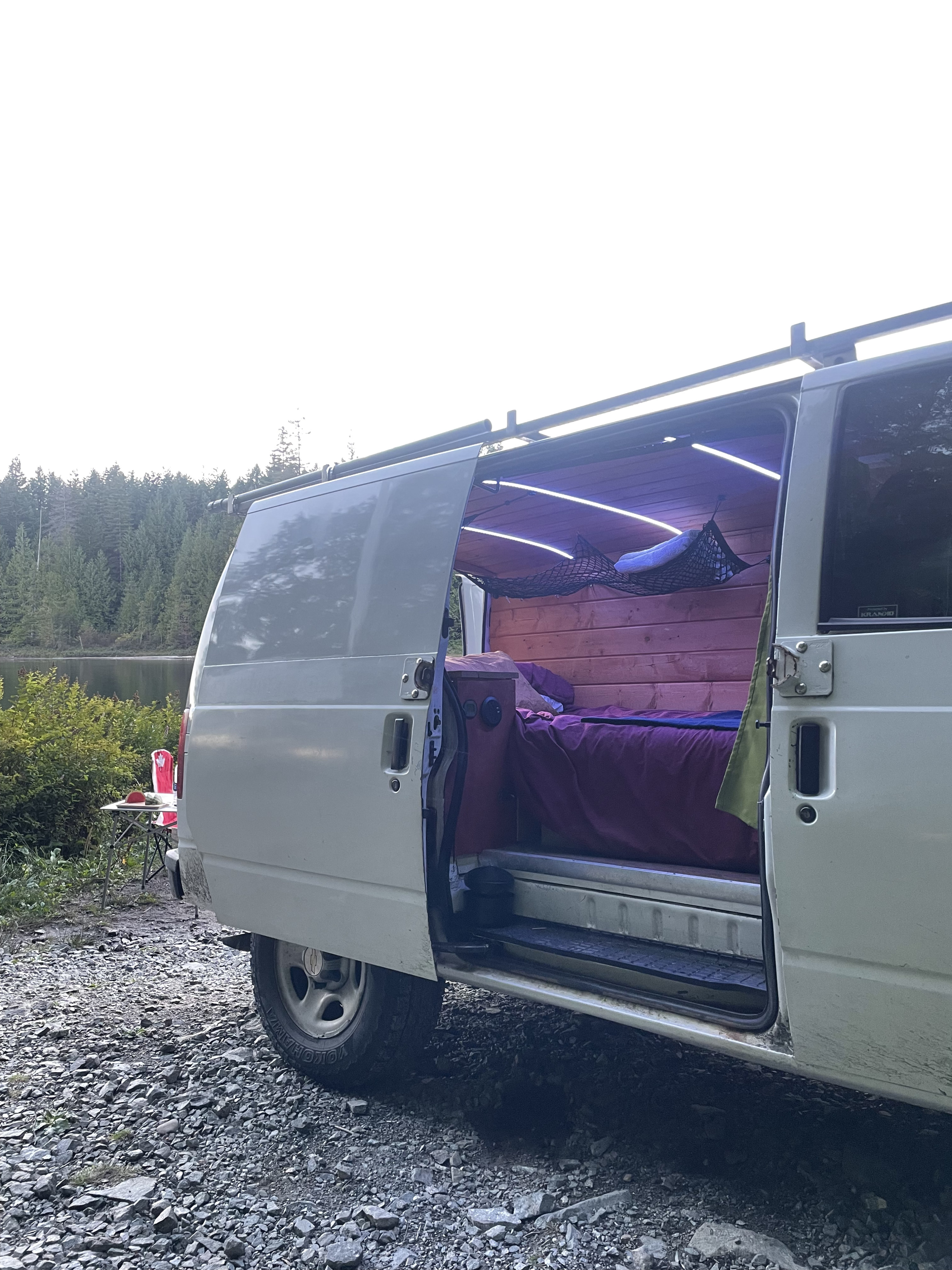 Cozy **rv rental** campervan interior with wood walls, LED lights, parked lakeside for a peaceful camping trip amidst a forest.. Chevy Astro 2004