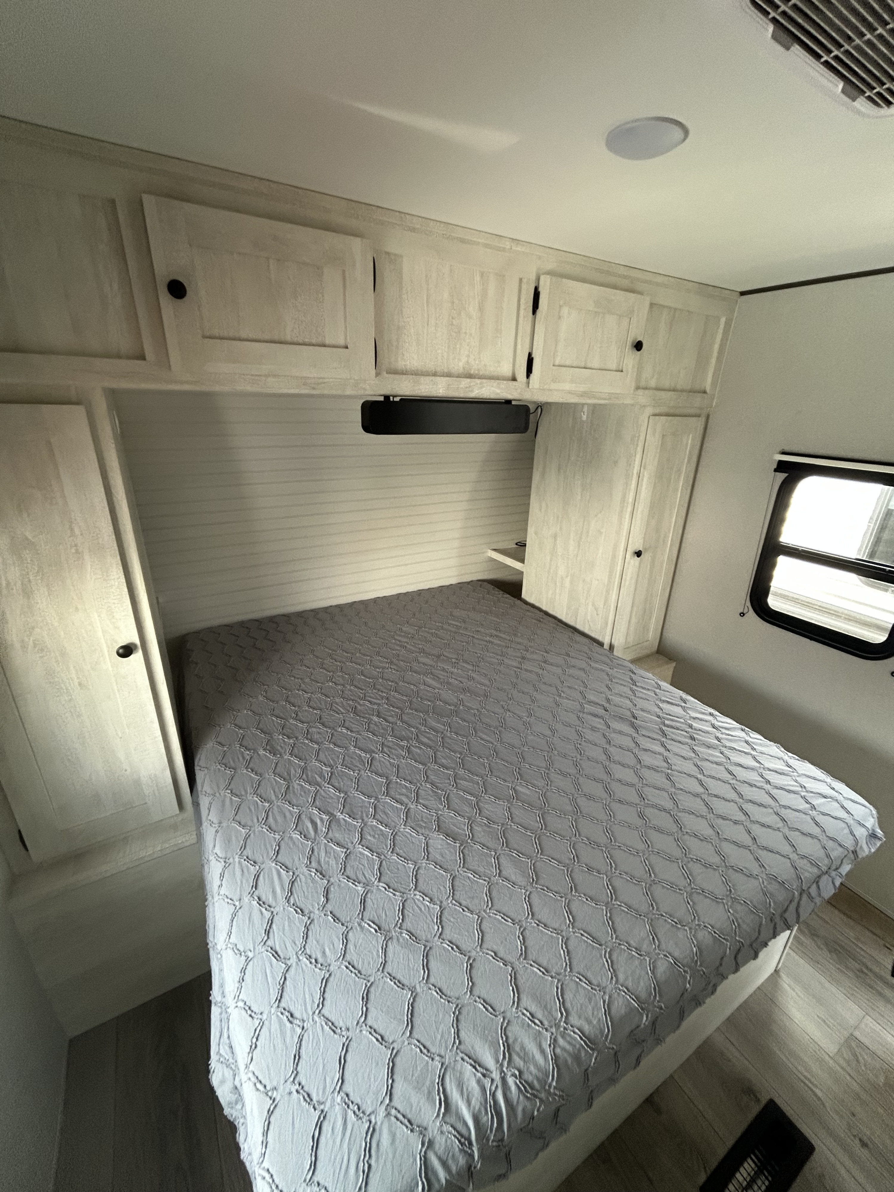 Cozy RV rental interior: A bedroom with a comfortable bed, gray textured comforter, and built-in wood-look cabinets.. Forest River Shasta i-5 2024