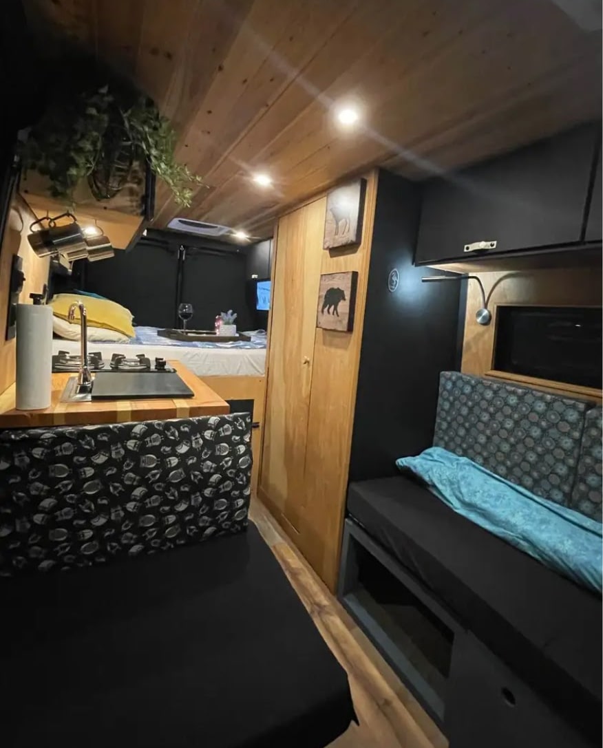 Spacious RV rental interior: full kitchen, comfy bed, & seating. Wood ceiling contrasts with sleek black accents.. Ram Pro Master 2017