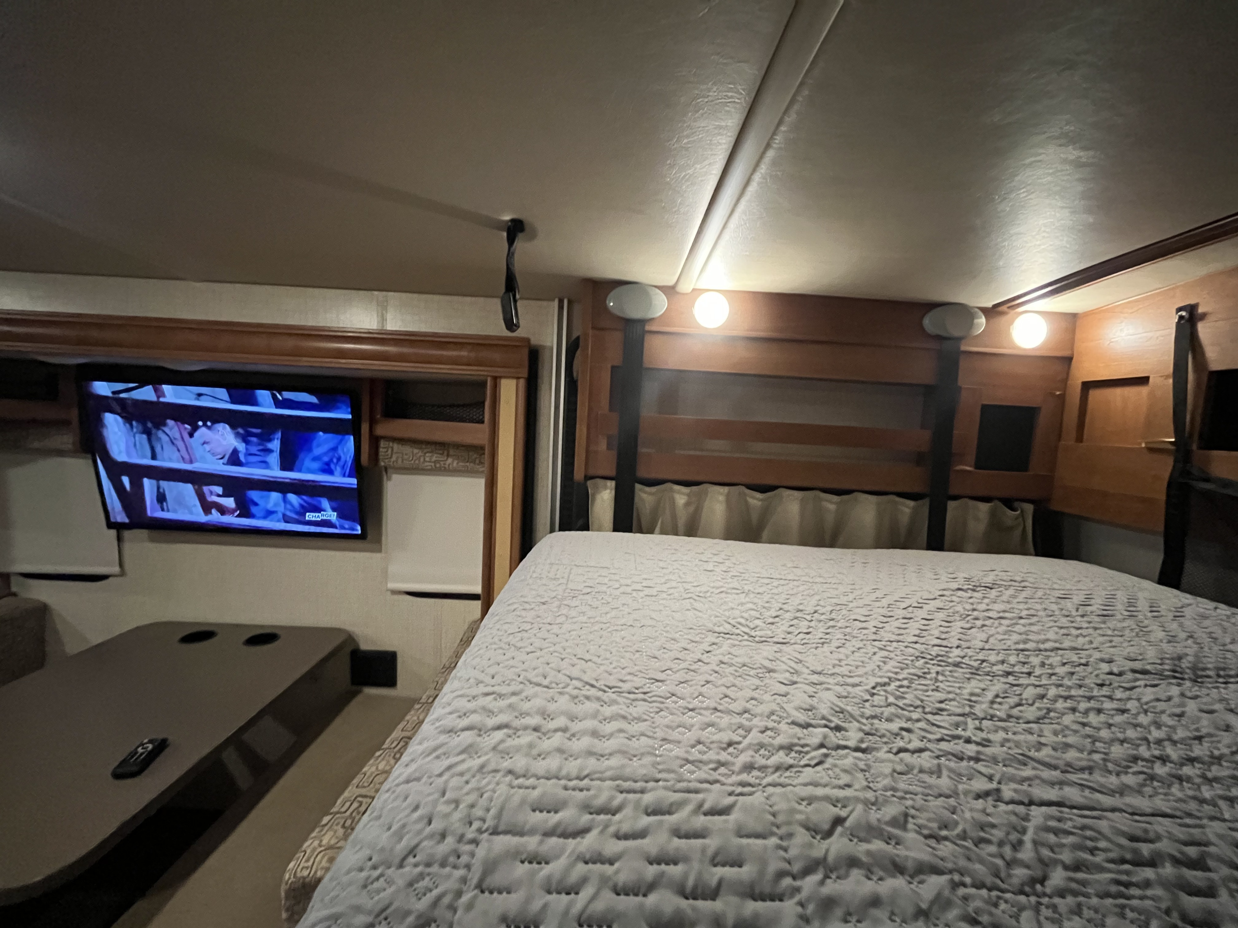 A detailed view inside an rv rental, showing a large, quilted bed, a TV playing a show, and a dinette with cup holders.. Winnebago Other 2018