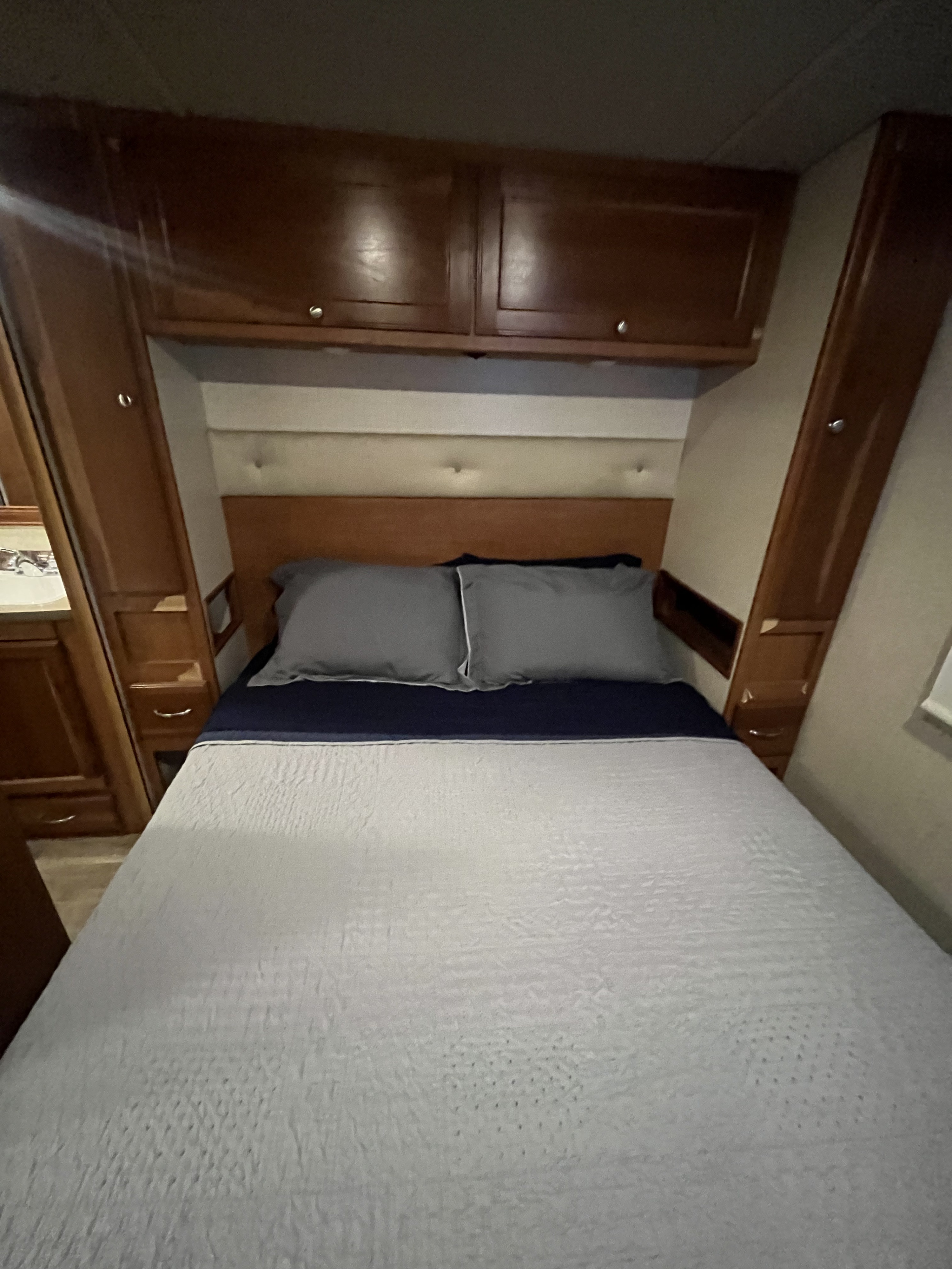 Compact RV rental bedroom featuring a bed, overhead cabinets, and side storage with a vanity sink.. Winnebago Other 2018