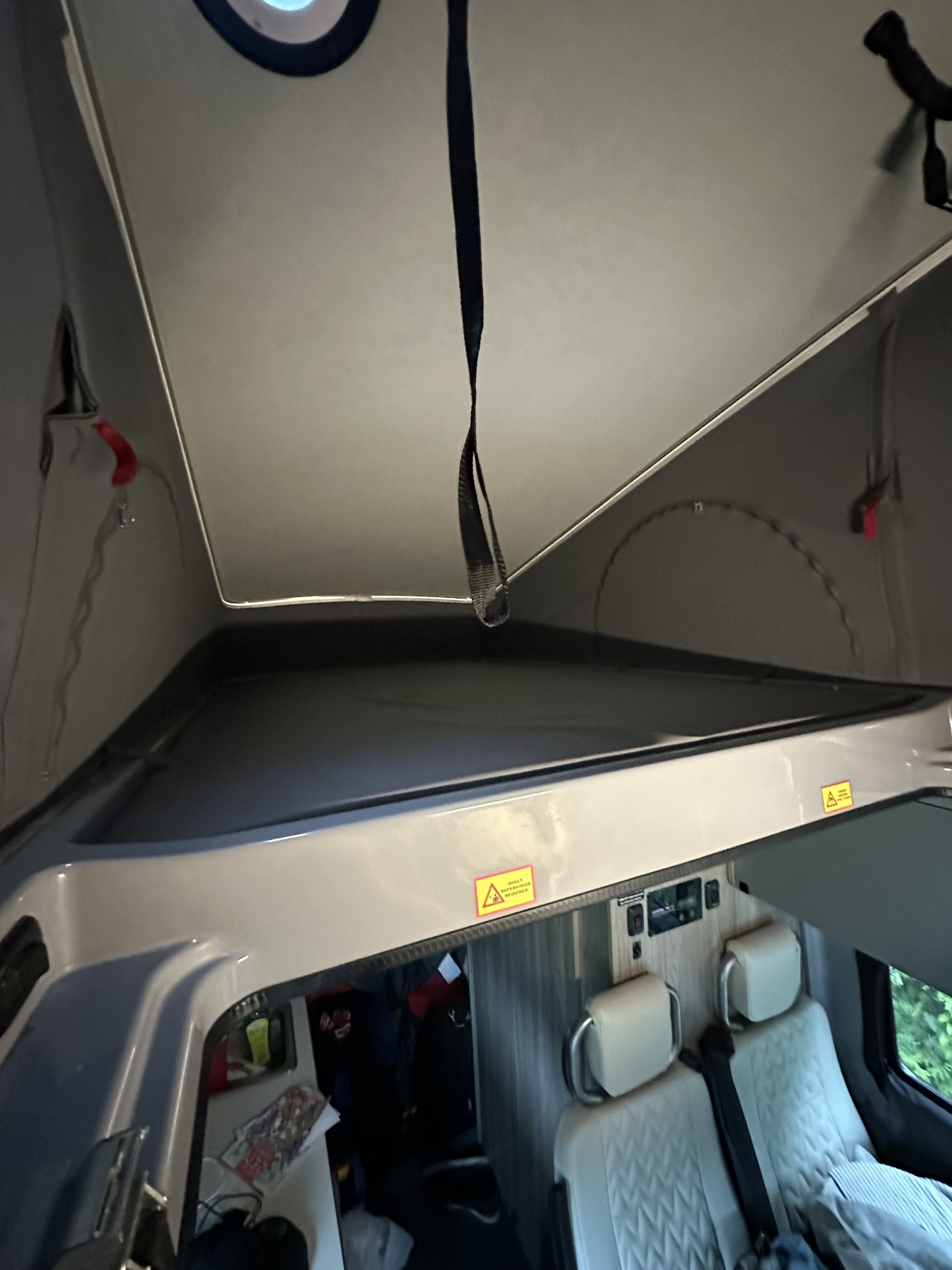 RV rental's pop-top open: elevated bed, pull strap, warning sign, and lower passenger cabin visible.. Winnebago Solis 2023