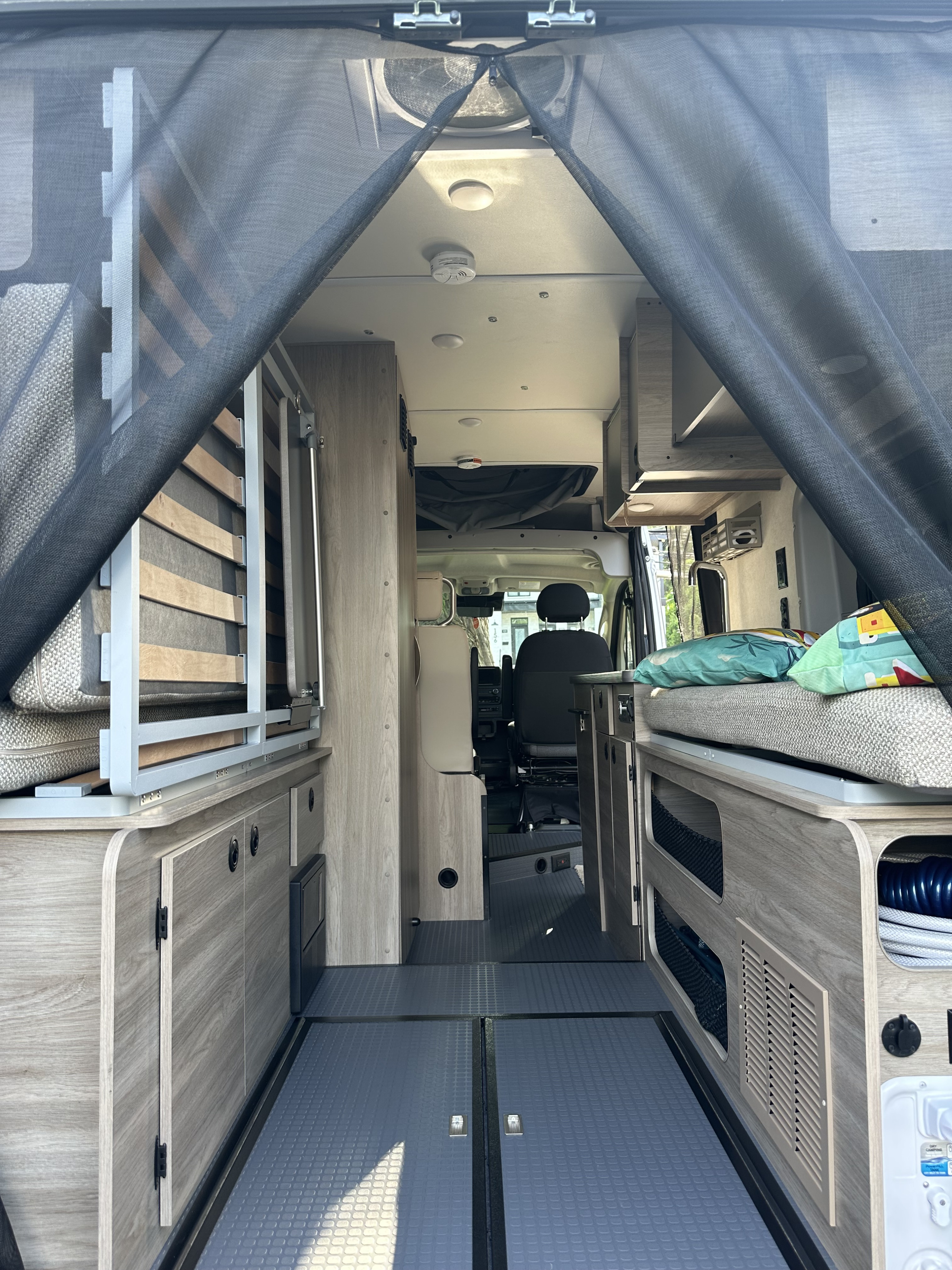 Step inside this RV rental! View of its modern interior, showcasing light wood storage, bed frames, and protective mesh screens.. Winnebago Solis 2023
