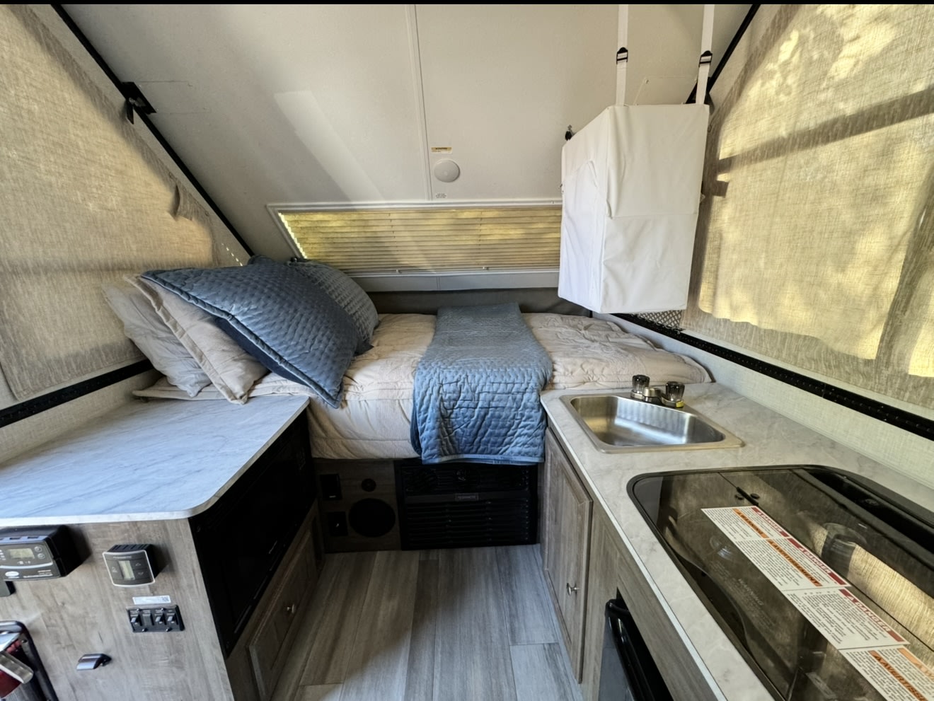 Compact RV rental interior featuring a cozy bed, kitchen with sink & stove, and control panel. Ideal for travel.. Forest River Rockwood LTD 2023