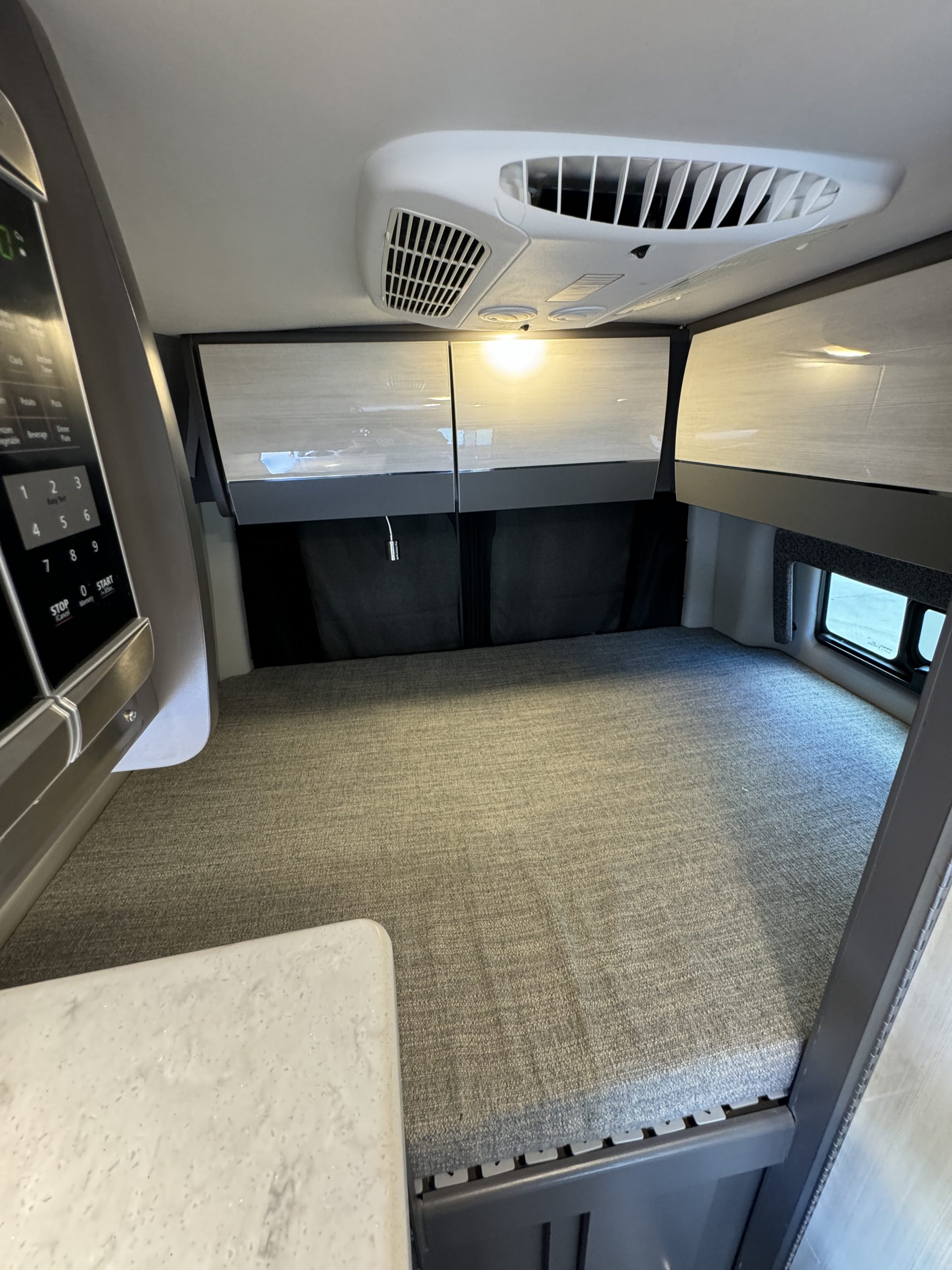 Cozy RV rental interior showcasing a comfortable bed, overhead storage, a microwave, and a ceiling AC unit for road trips.. Mercedes Sprinter 2022