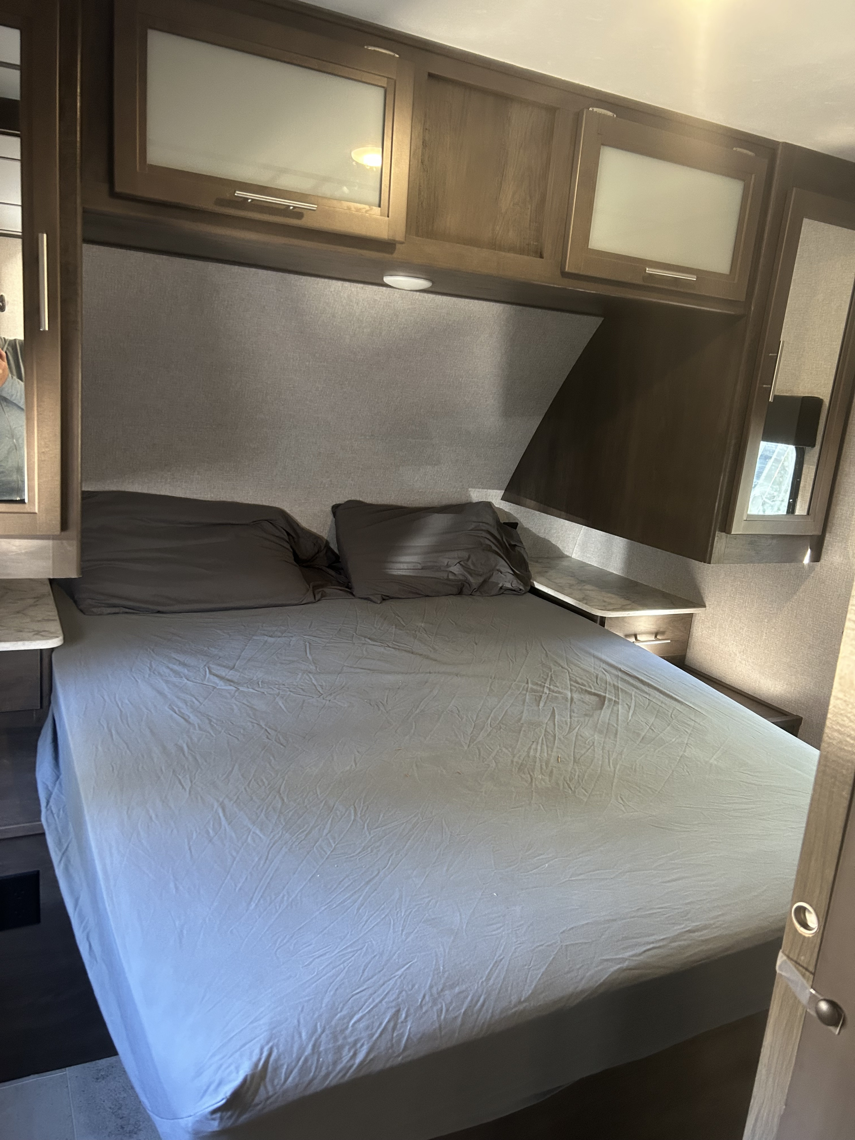 This RV rental bedroom features a comfortable bed, upholstered headboard, overhead storage cabinets, and bedside shelves.. Dutchmen CM2455BH20 2020