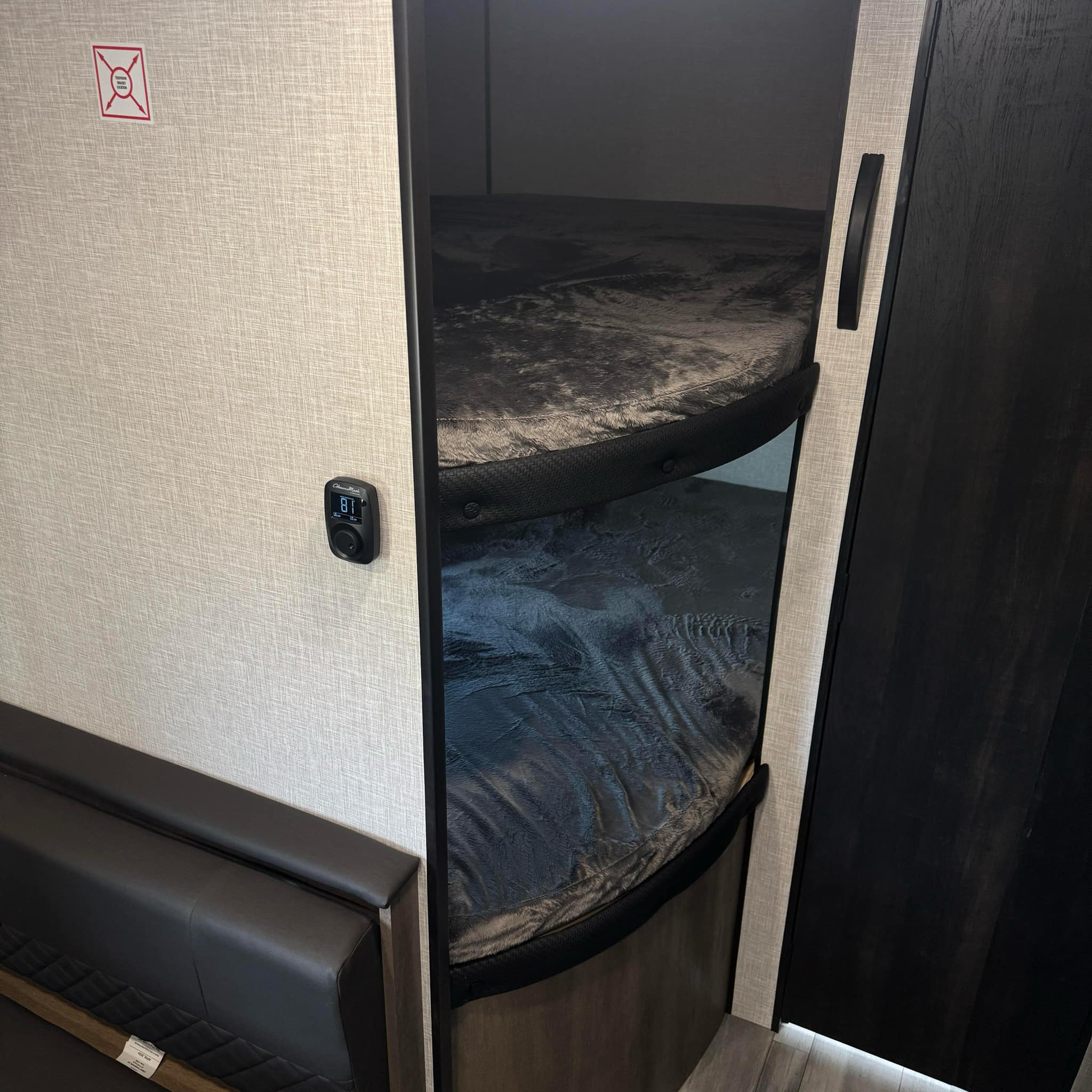 Inside an RV rental, revealing cozy bunk beds with dark bedding, a digital thermostat reading 81, and textured interior walls.. Jayco Jay Flight SLX 2024