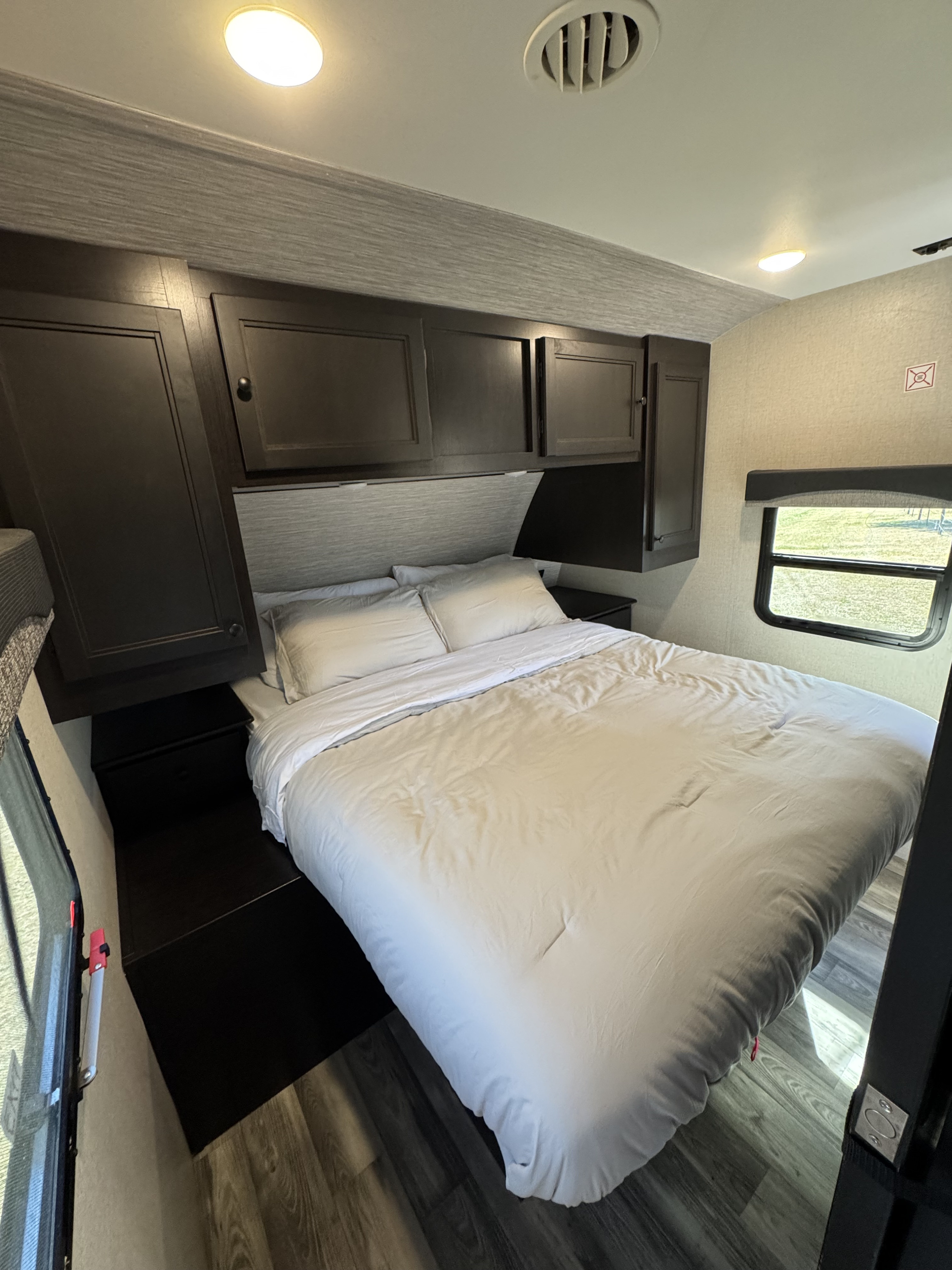 Cozy RV rental bedroom featuring a comfortable bed with light bedding, dark wood cabinets, and a window for natural light.. Highland Ridge RV Range Lite 2022