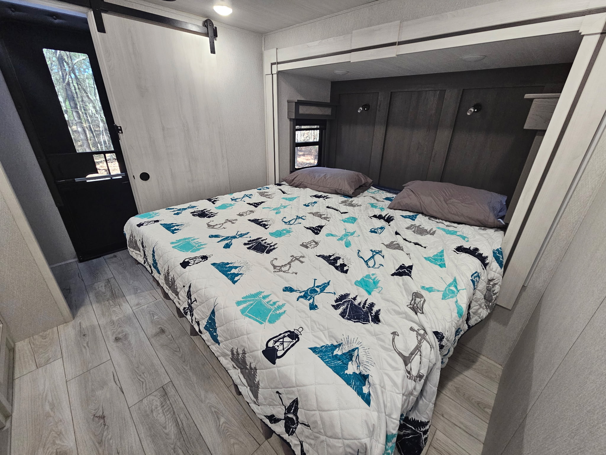 Bright, modern RV rental bedroom featuring a patterned quilt on the bed, light wood floor, and a sleek sliding barn door.. Forest River East to West Ahara 390DS 2025