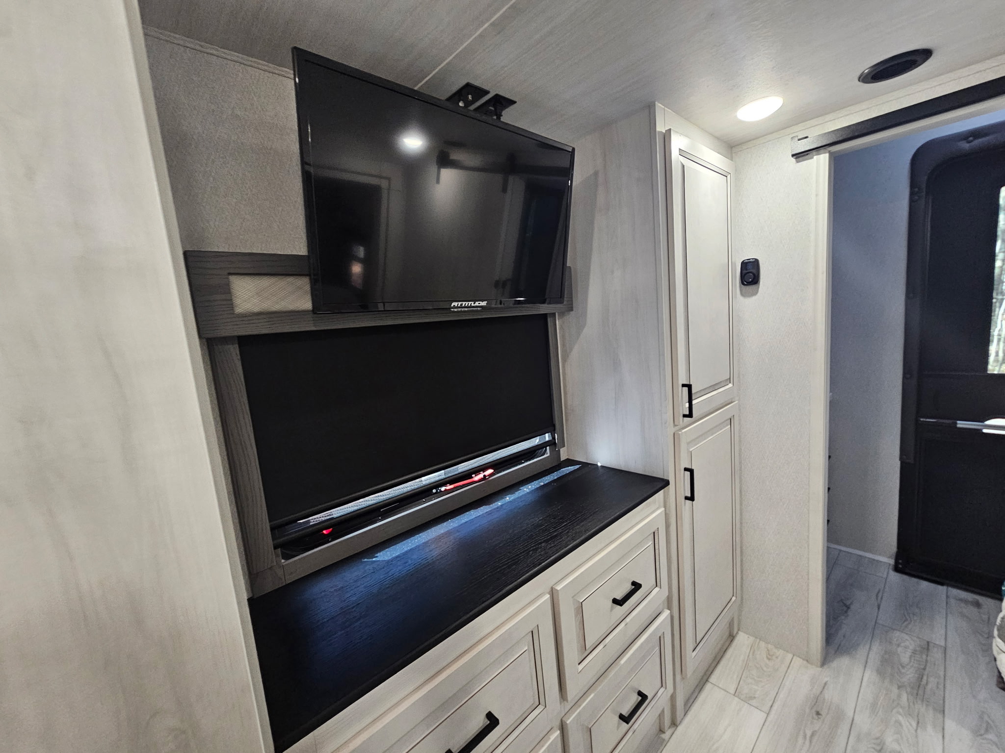 Inside a modern RV rental: flat-screen TV, a lower entertainment unit, drawers, and tall cabinet storage.. Forest River East to West Ahara 390DS 2025