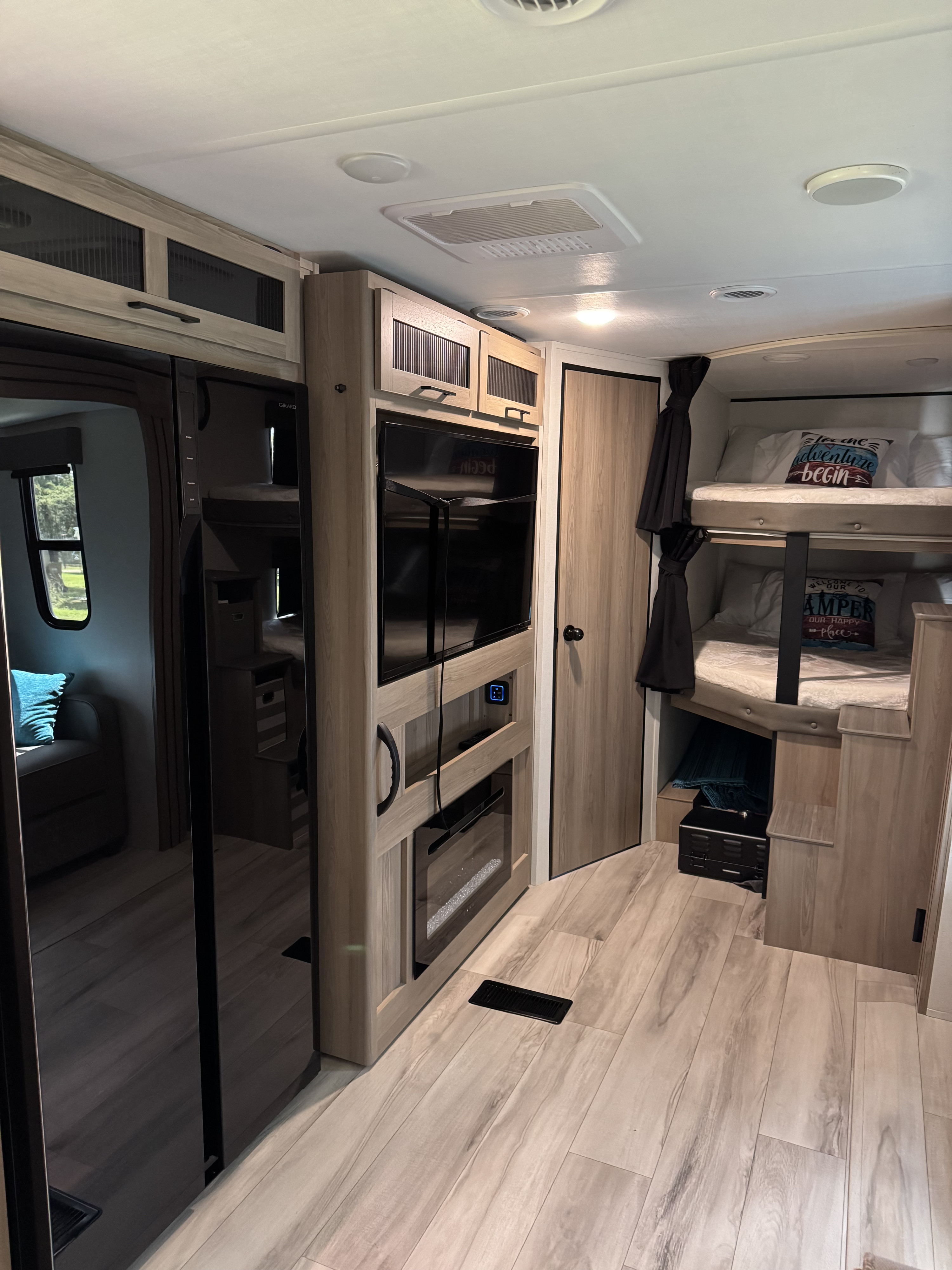 Modern RV rental interior features a fridge, entertainment center with fireplace, and comfy bunk beds. Light wood flooring and bright design.. Keystone Coleman Legacy 2900BH 2025