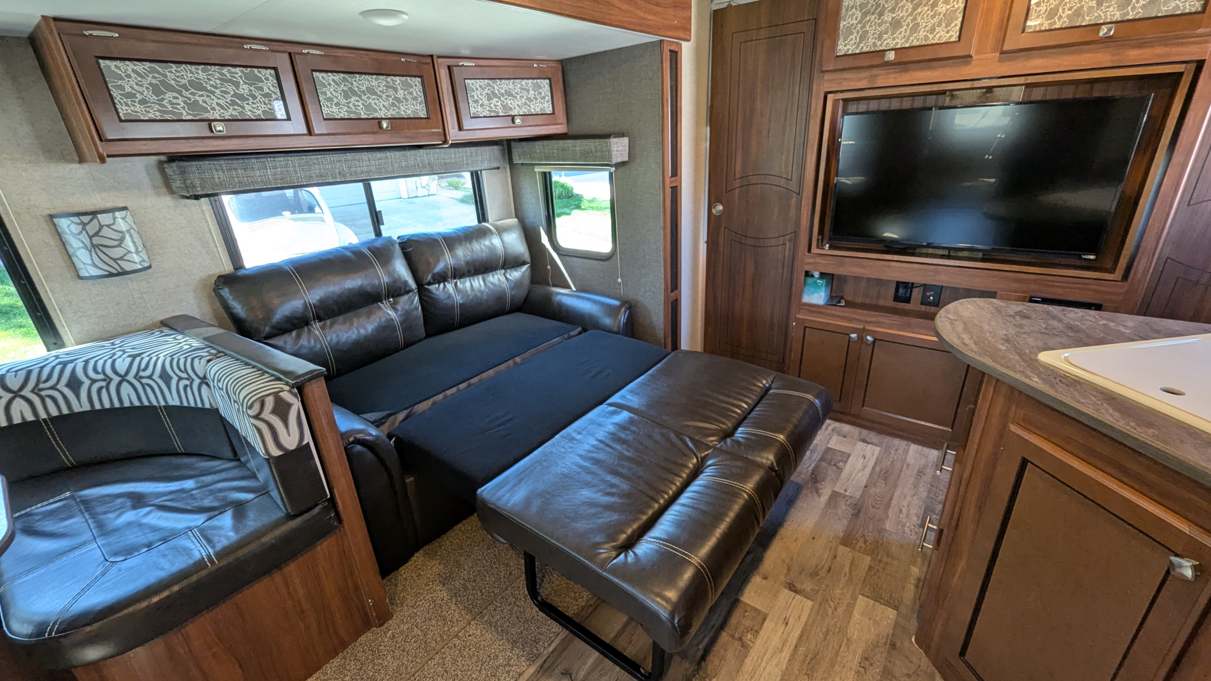 Spacious RV rental living area featuring a sofa bed, comfy dinette, kitchen, TV, and overhead storage.. Heartland RVs Mallard 2017