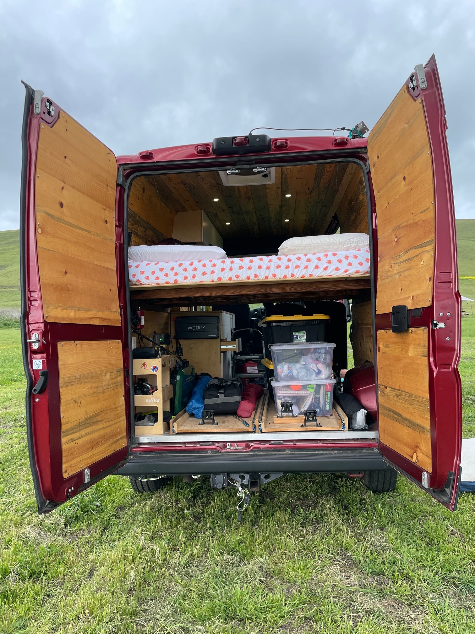 Rear view of custom red camper van, doors open, showing bed and storage. Ideal for rv rental and van life adventures in nature.. Dodge Ram Promaster 2020