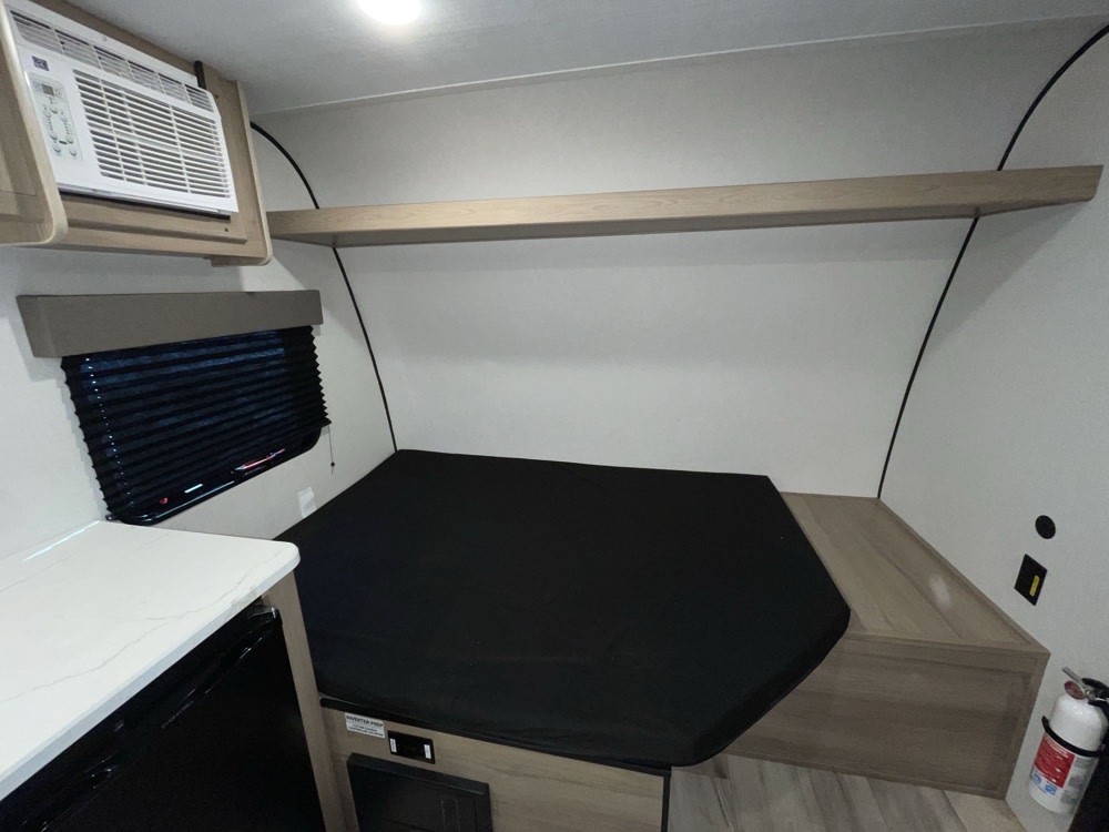 Compact RV rental interior featuring a bed, AC unit, window, and countertop, ready for travel.. Keystone RV Coleman 13B 2025